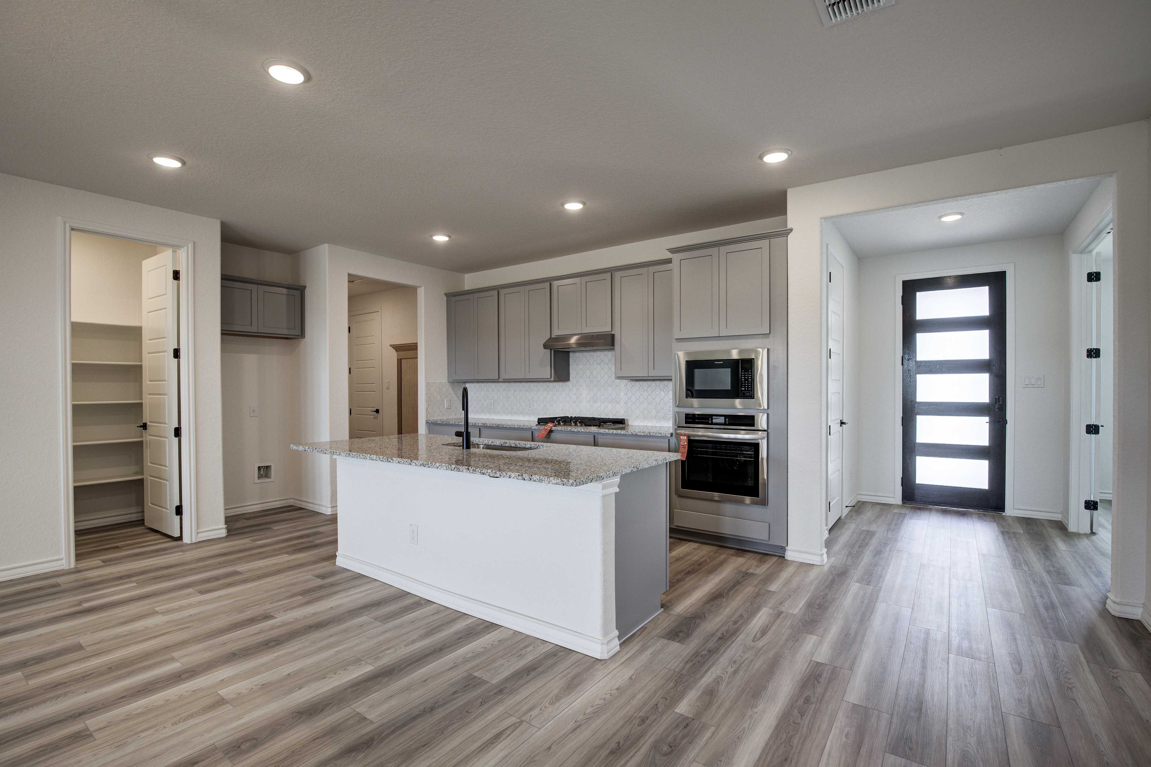 Spacious kitchen in The Lanier home plan with gray cabinets, white granite island, stainless appliances, open pantry, hardwood floors