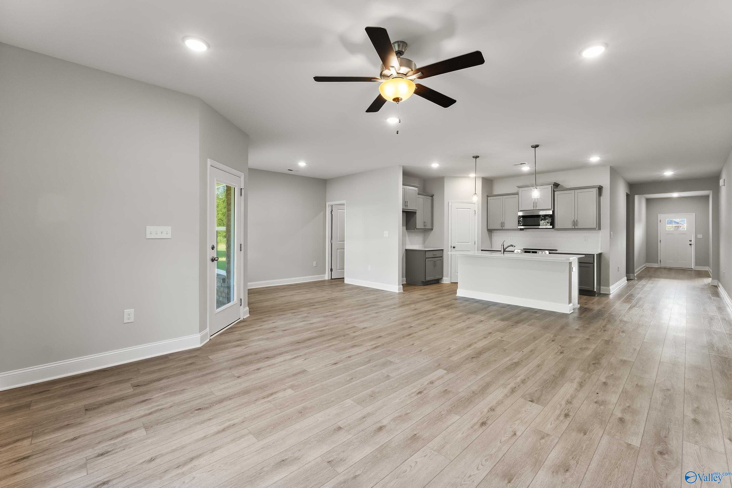 Open-concept kitchen-living space with hardwood floors, white cabinetry, stainless appliances, and ceiling fan in Davidson Homes The Daphne C, Huntsville AL
