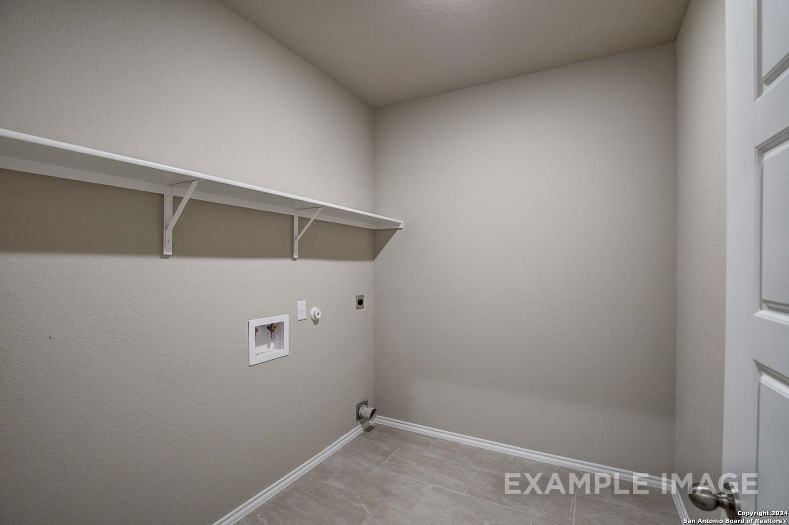 Spacious laundry room with built-in white shelving, washer dryer hookups, and tiled flooring in Davidson Homes The Murray J, Bricewood, San Antonio