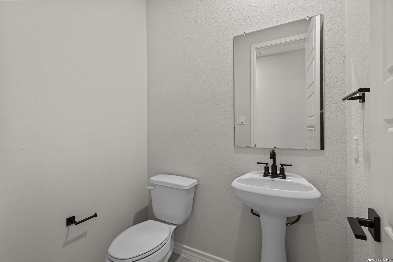 Elegant half bath with pedestal sink, black fixtures, and framed mirror in Davidson Homes The Oxford F, Castroville, Texas