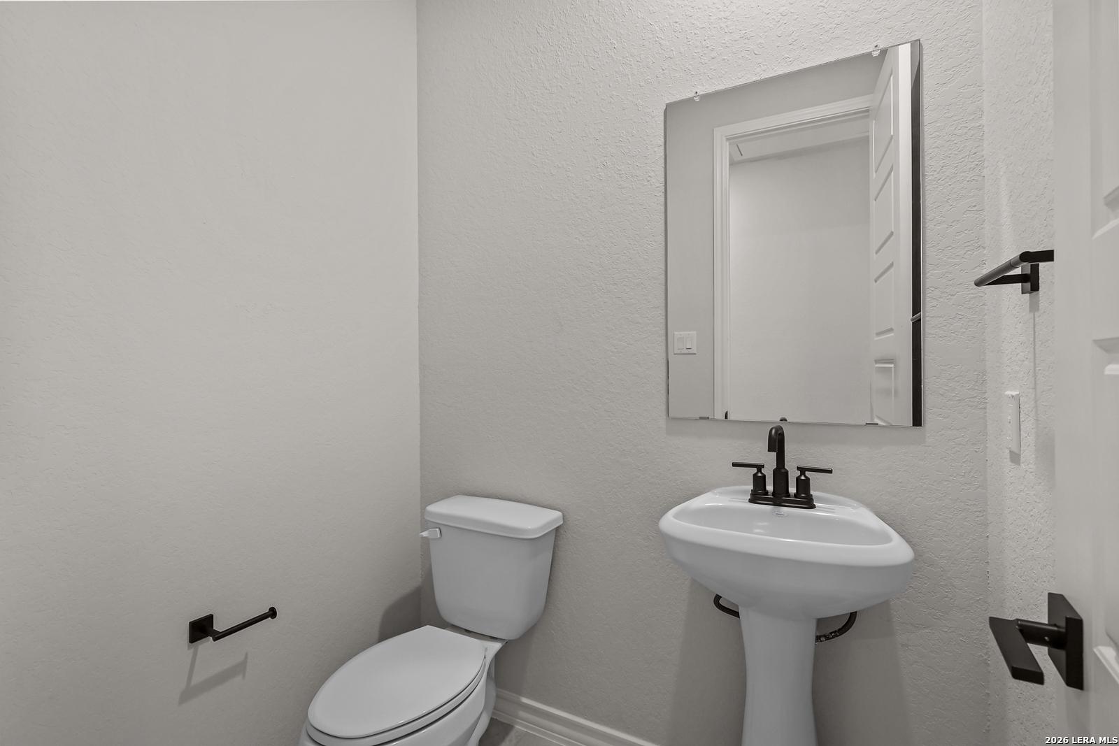 Elegant half bath with pedestal sink, black fixtures, and framed mirror in Davidson Homes The Oxford F, Castroville, Texas