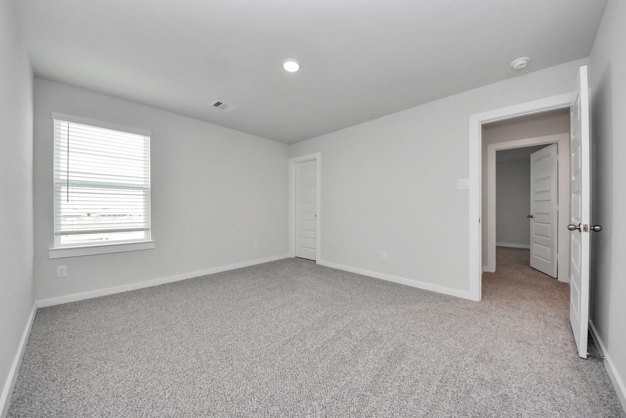 Bright empty bedroom with gray carpet, window with blinds, and white doors in The San Marcos E floor plan, Emberly, Beasley, Texas