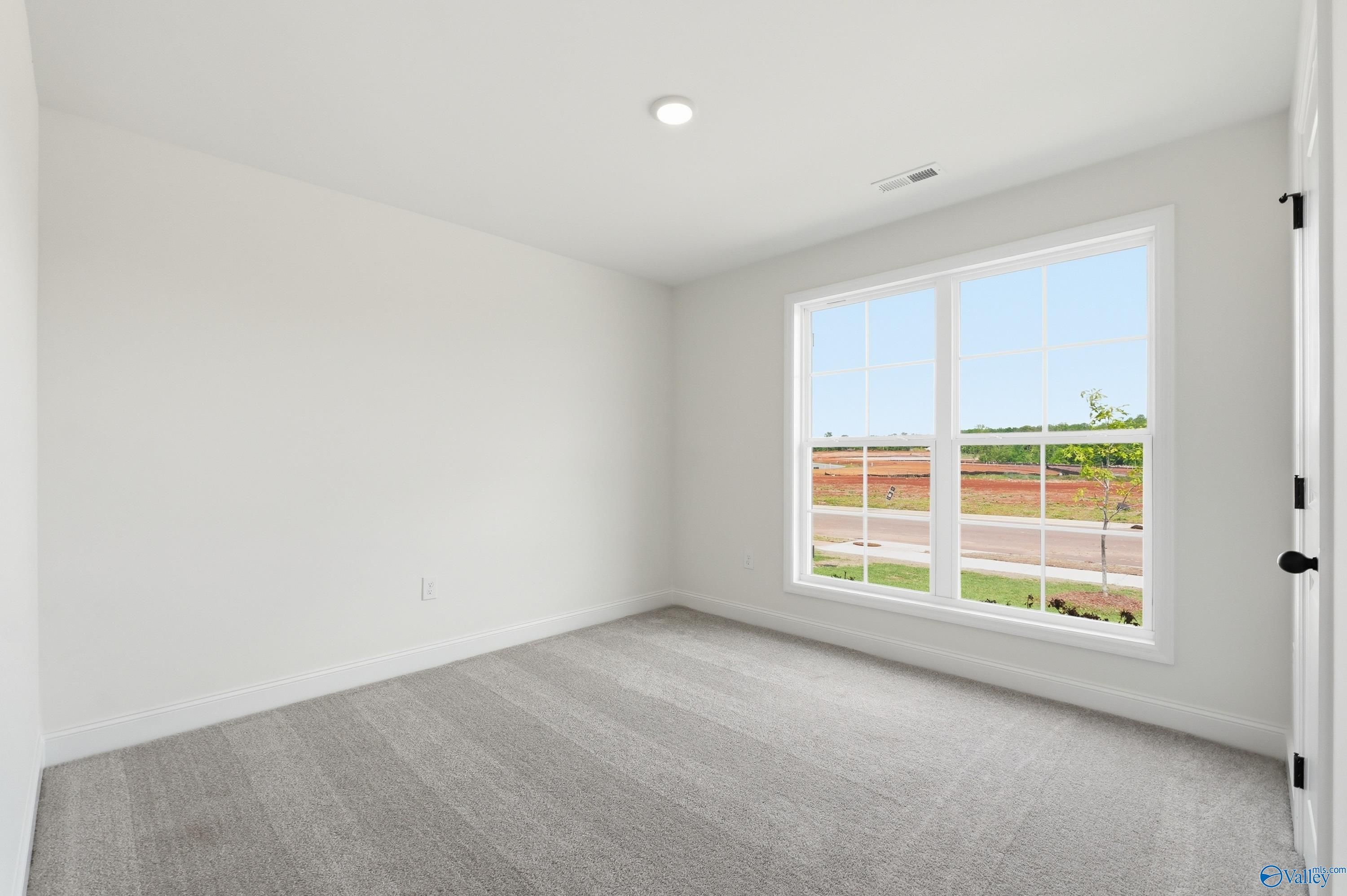 Bright bedroom with neutral carpet and large window in The Franklin floor plan at Heritage Lakes, New Market, Alabama.