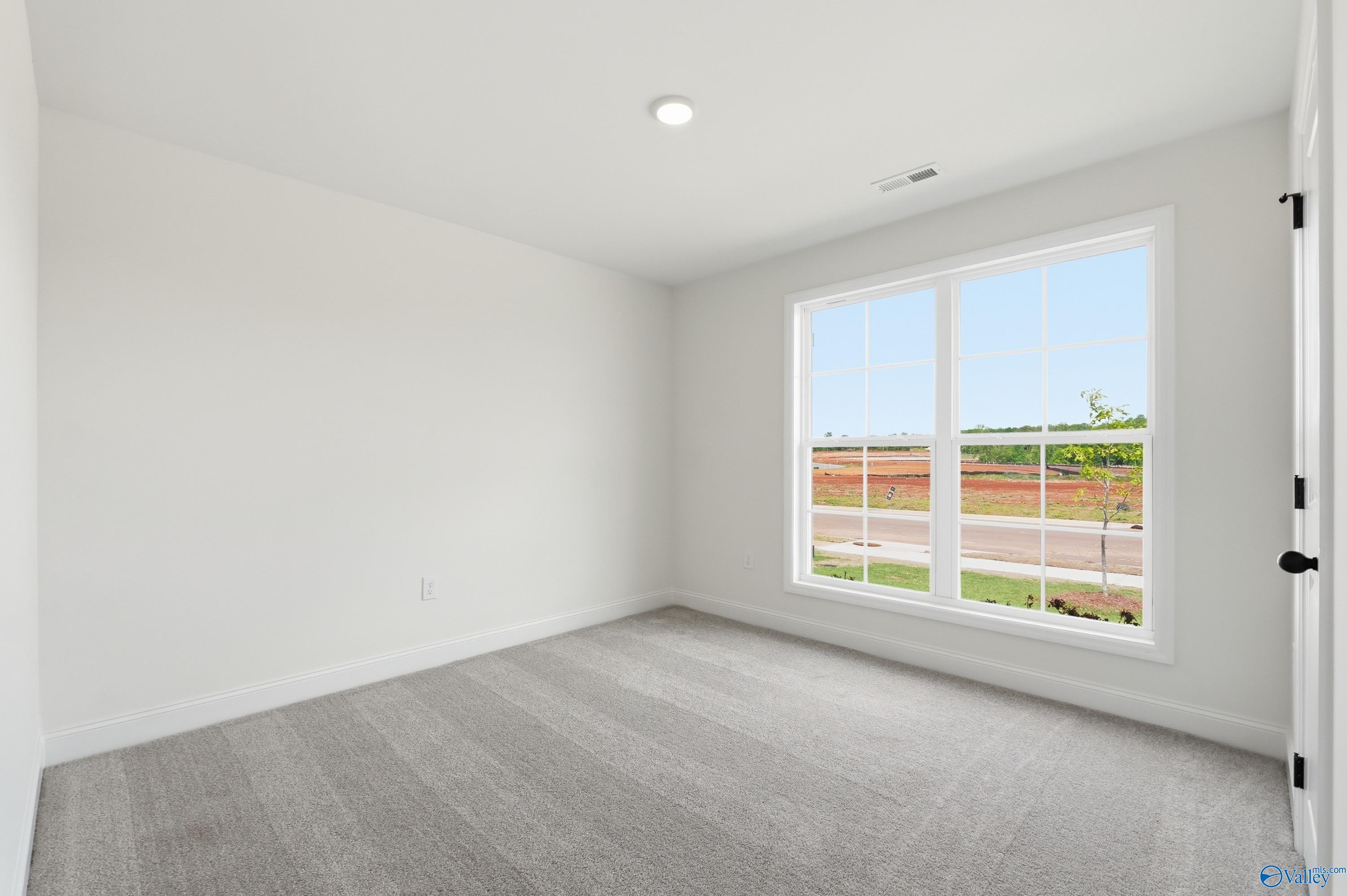 Bright bedroom with neutral carpet and large window in The Franklin floor plan at Heritage Lakes, New Market, Alabama.