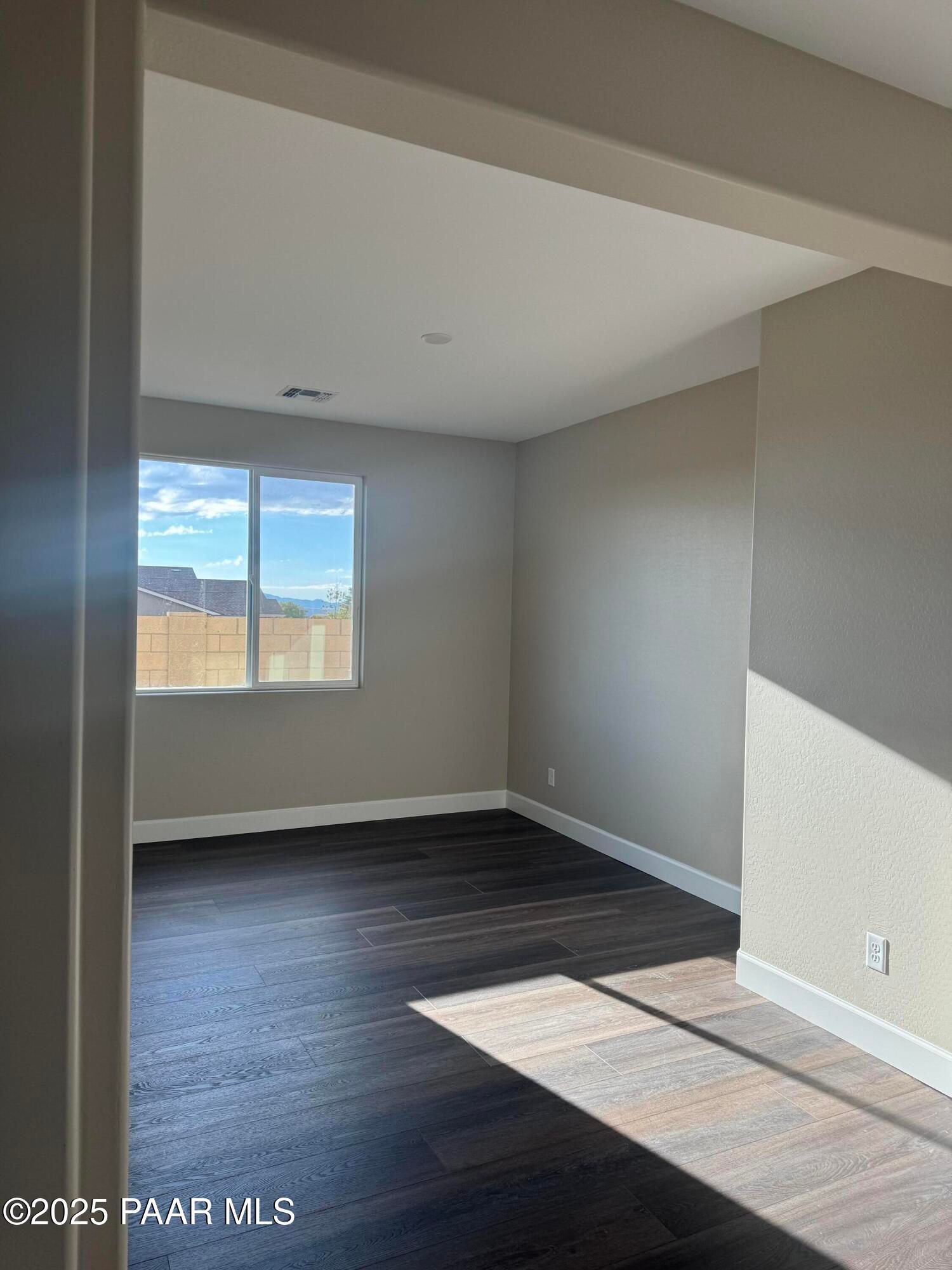 Sunlit bedroom with mountain view through large window, beige walls, and dark hardwood floors in Evermore Homes Sunrise A, Prescott Valley