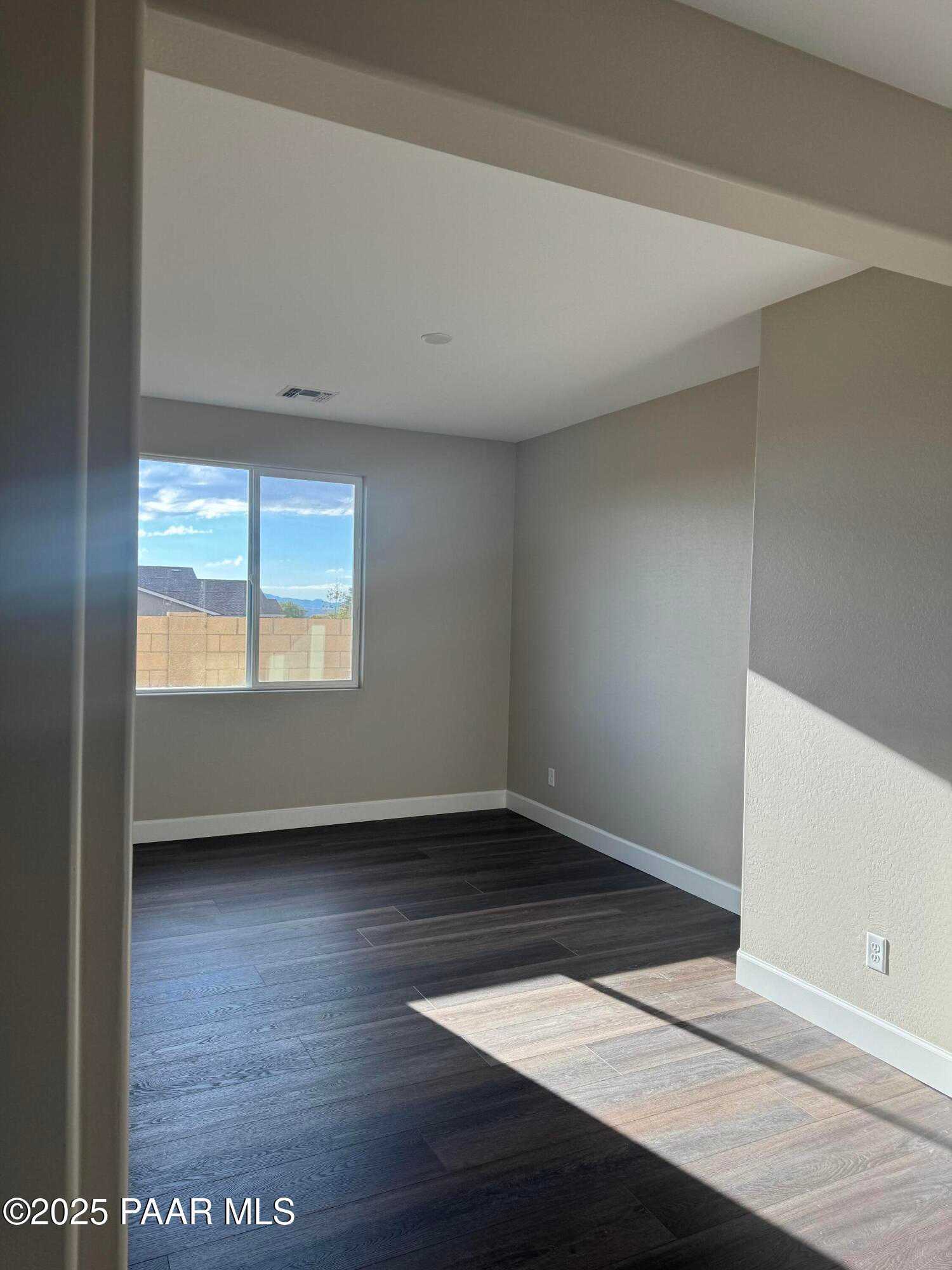 Sunlit bedroom with mountain view through large window, beige walls, and dark hardwood floors in Evermore Homes Sunrise A, Prescott Valley
