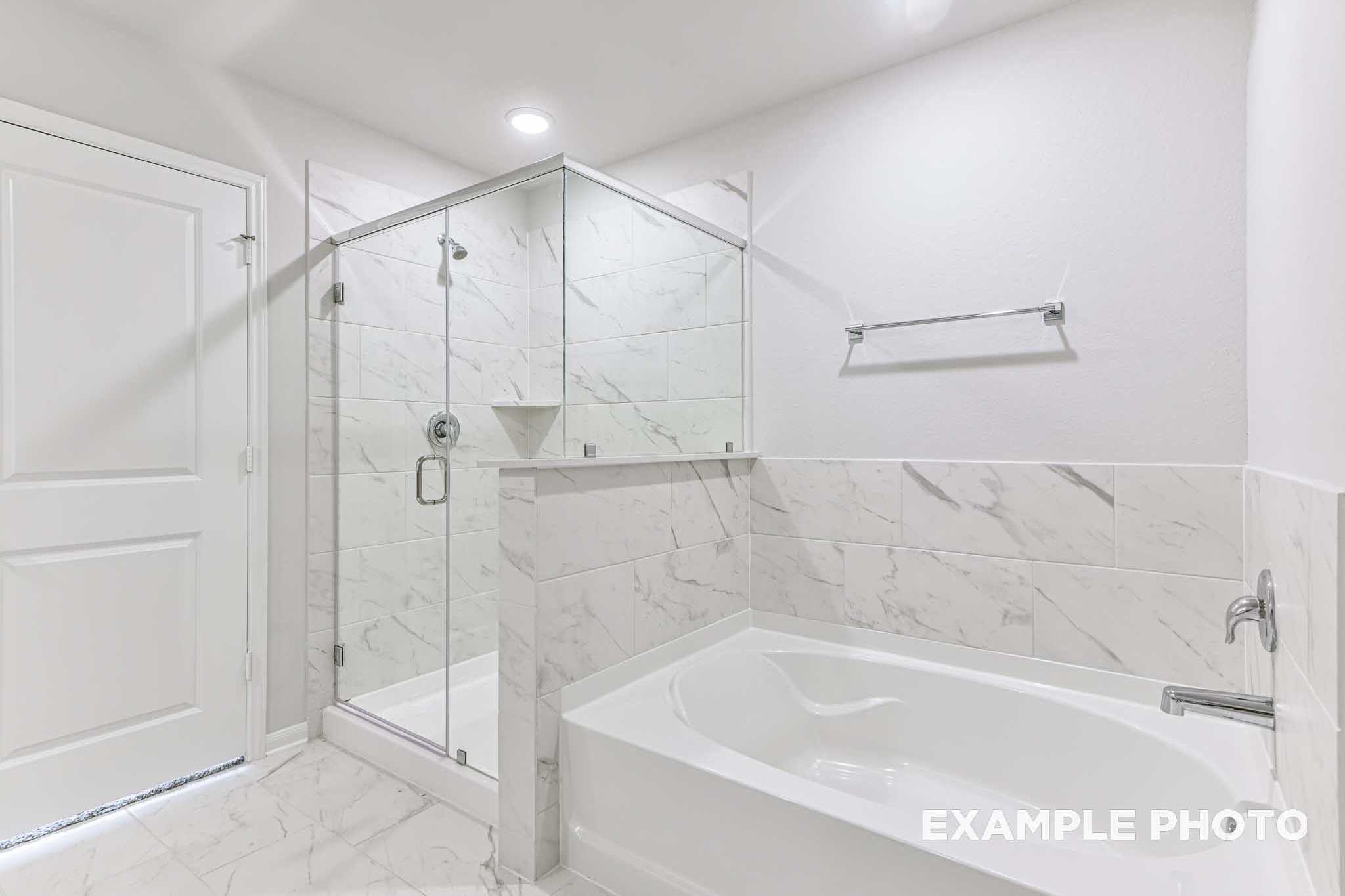 Spacious master bathroom in The Laguna B featuring frameless glass walk-in shower, marble tile accents, and deep soaking tub