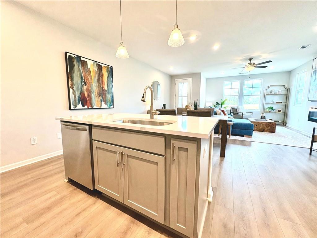 Open-concept kitchen with quartz island, stainless dishwasher, and gray cabinets flowing into living room in The Monroe A, Emerson, GA