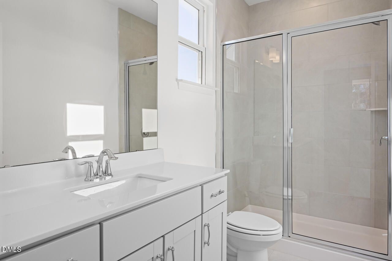 Modern master bathroom featuring white double vanity, frameless glass shower, and window in Davidson Homes The Cypress B II, Angier, NC