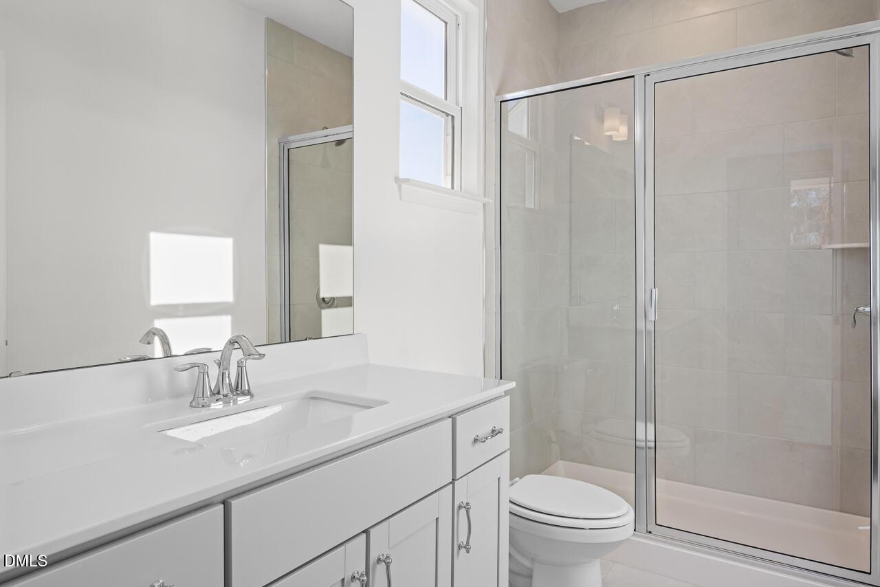Modern master bathroom with white double vanity, glass shower enclosure, and window in Davidson Homes The Cypress B II, Angier, NC