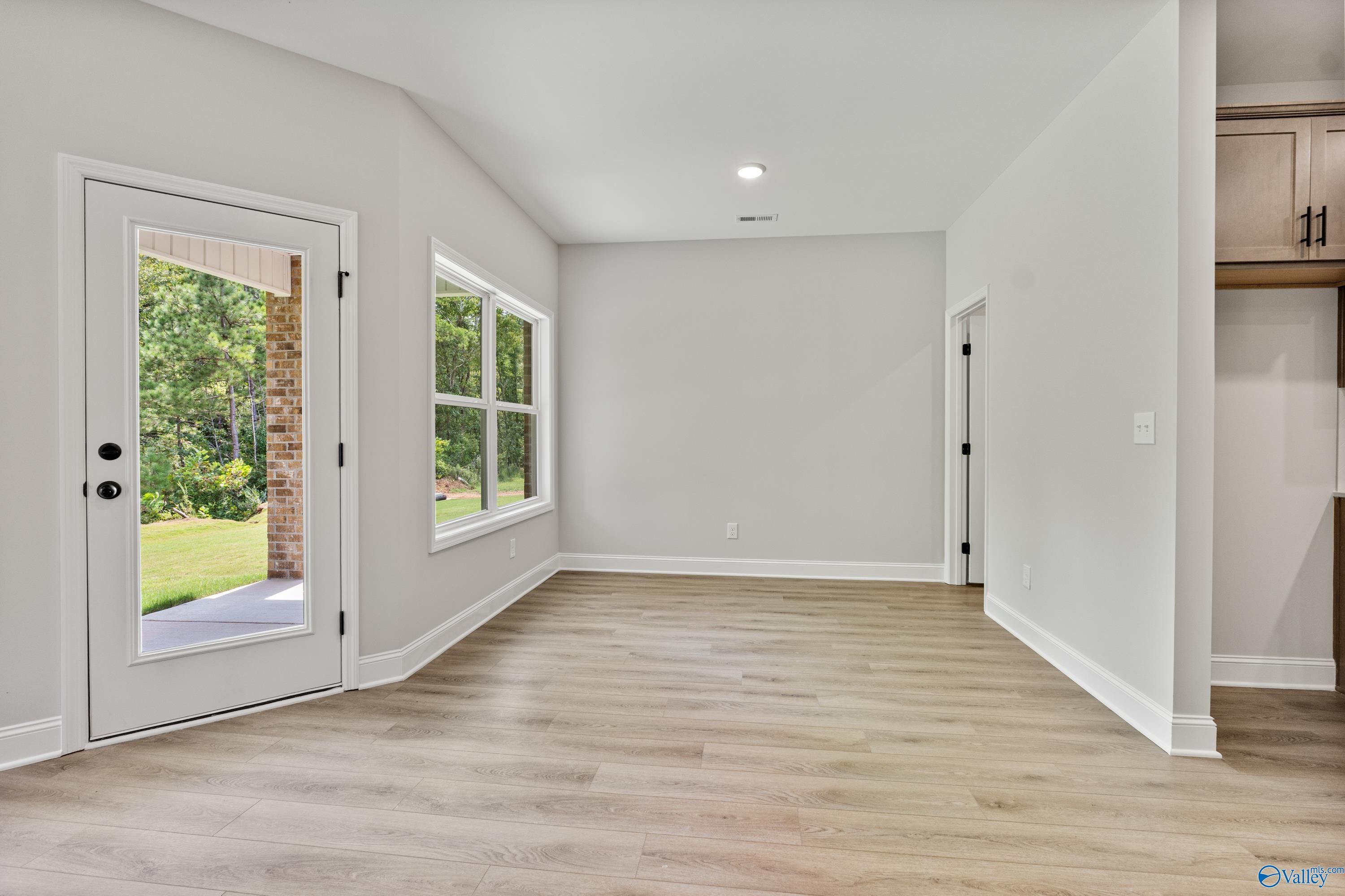 Bright living room with light wood floors, large windows, and glass door to green backyard in The Daphne floor plan, Huntsville AL
