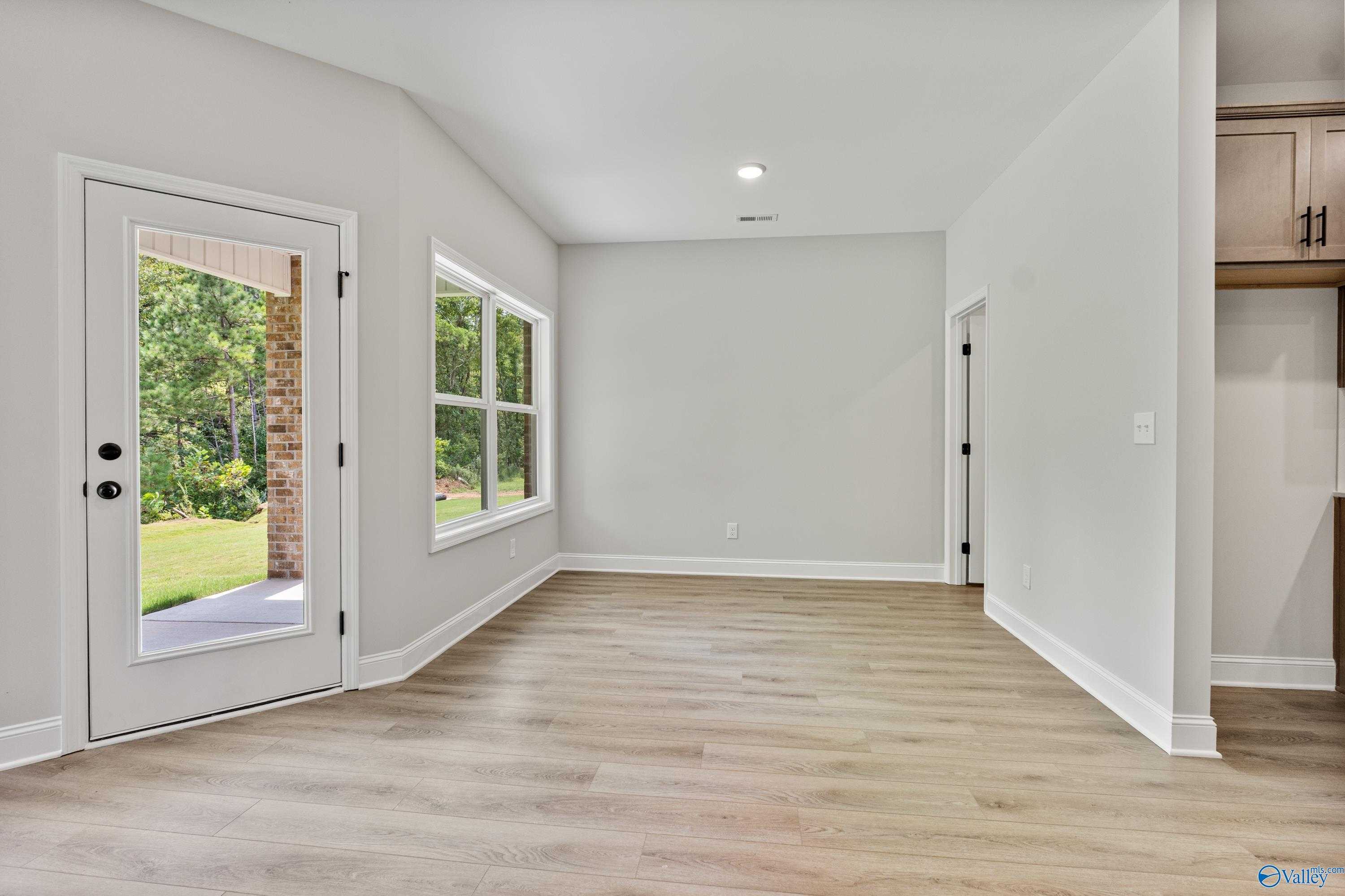 Bright living room with light wood floors, large windows, and glass door to green backyard in The Daphne floor plan, Huntsville AL