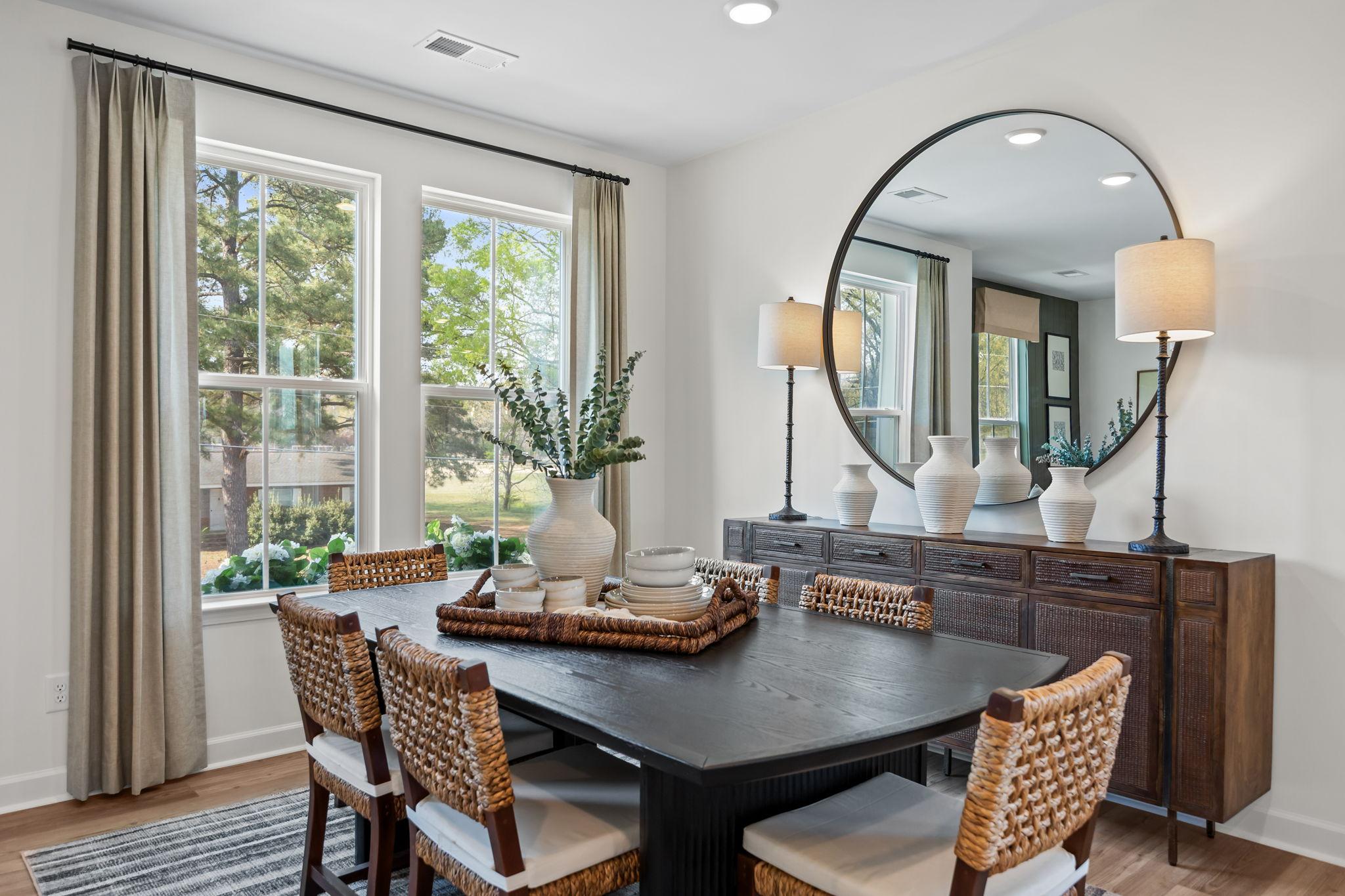 Elegant dining room in Camden Park Knightdale NC with black wood table, wicker chairs, large round mirror, and buffet with vases