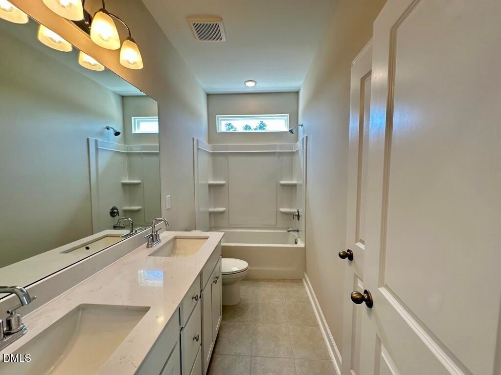 Elegant bathroom with double quartz vanity, soaking tub, shower, and neutral tile in Davidson Homes The Burke, Knightdale, NC