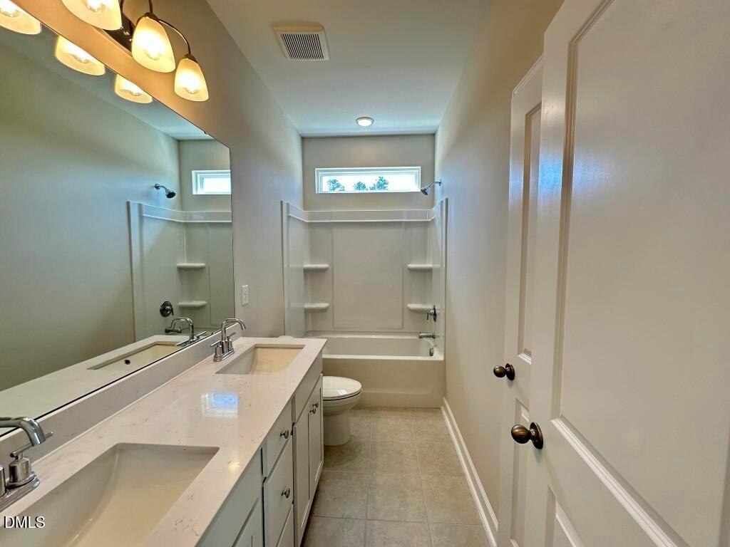 Elegant bathroom with double quartz vanity, soaking tub, shower, and neutral tile in Davidson Homes The Burke, Knightdale, NC