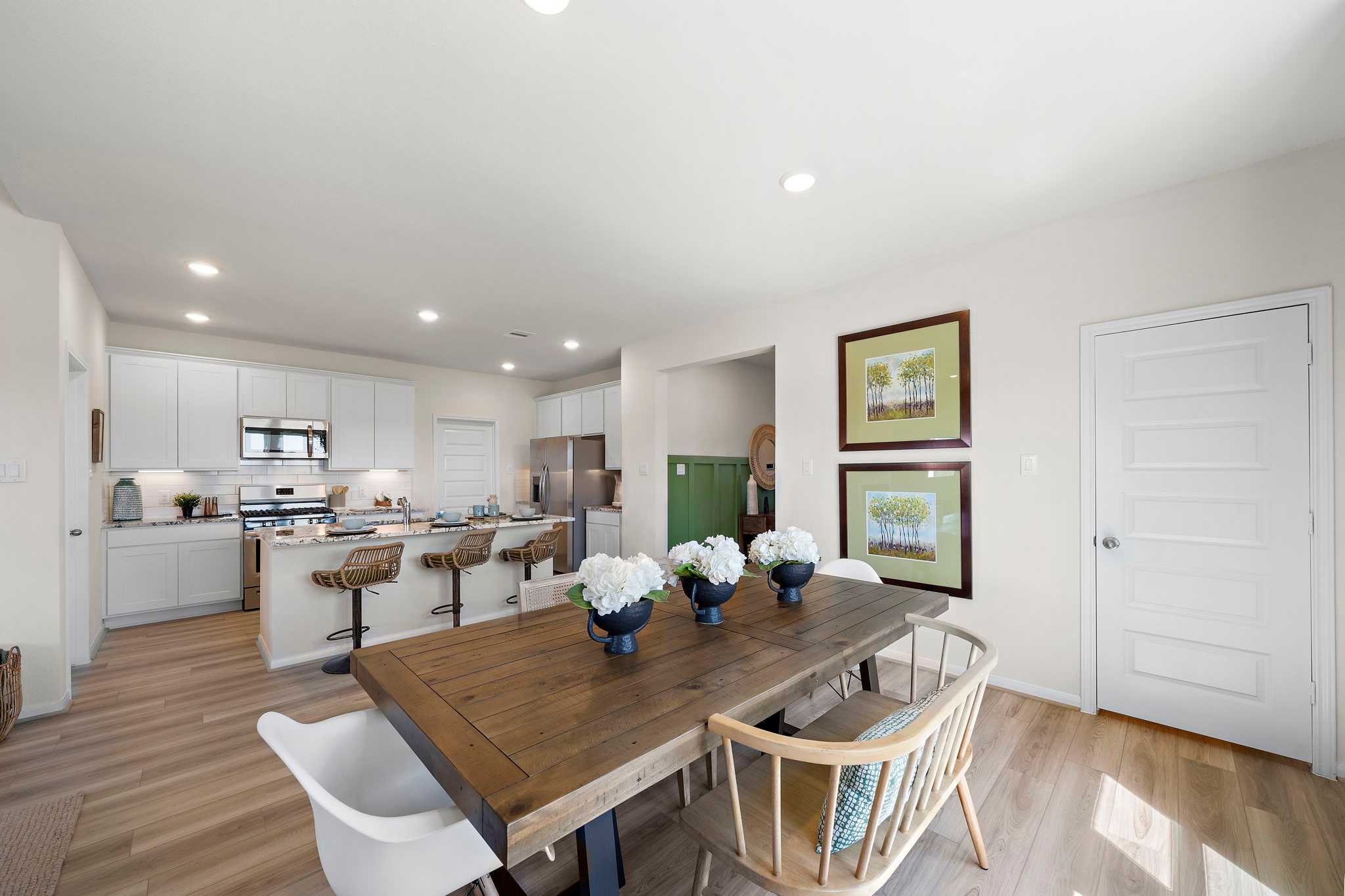 Spacious open-concept kitchen dining area at River Ranch Meadows in Dayton Texas with white cabinets island bar stools and wooden farmhouse table