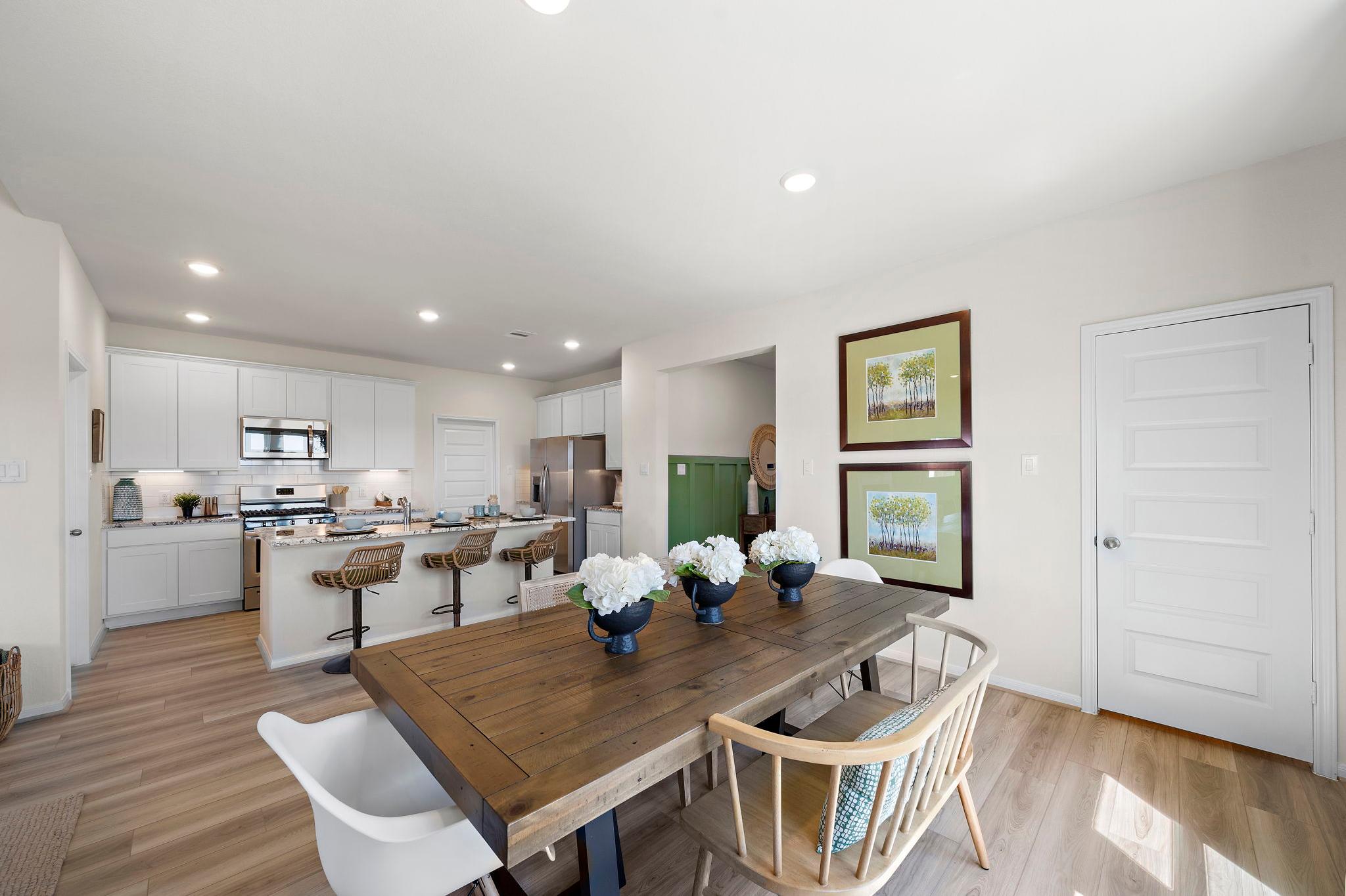 Spacious open-concept kitchen dining area at River Ranch Meadows in Dayton Texas with white cabinets island bar stools and wooden farmhouse table