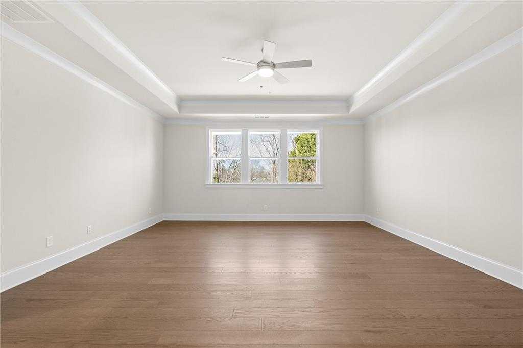 Spacious empty bedroom with hardwood floors, tray ceiling, ceiling fan, and large windows in Davidson Homes The Arlington A, East Cobb