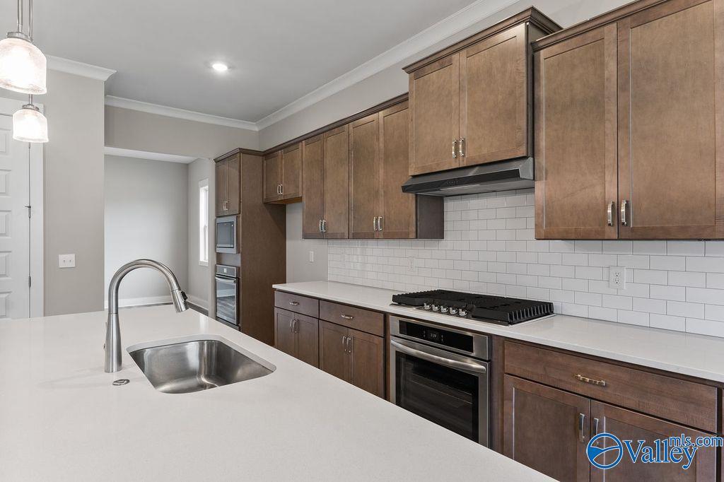 Modern kitchen with warm wood cabinets, white quartz counters, subway tile backsplash, stainless gas cooktop in Evermore Homes The Oxford, Owens Cross Roads, AL