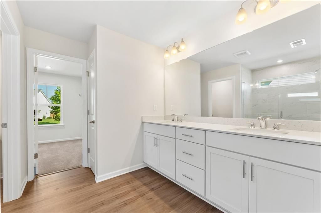 Modern double vanity bathroom with white cabinets, large mirror, and wood flooring in Davidson Homes The Willow B, Riverwood, Dallas, Georgia