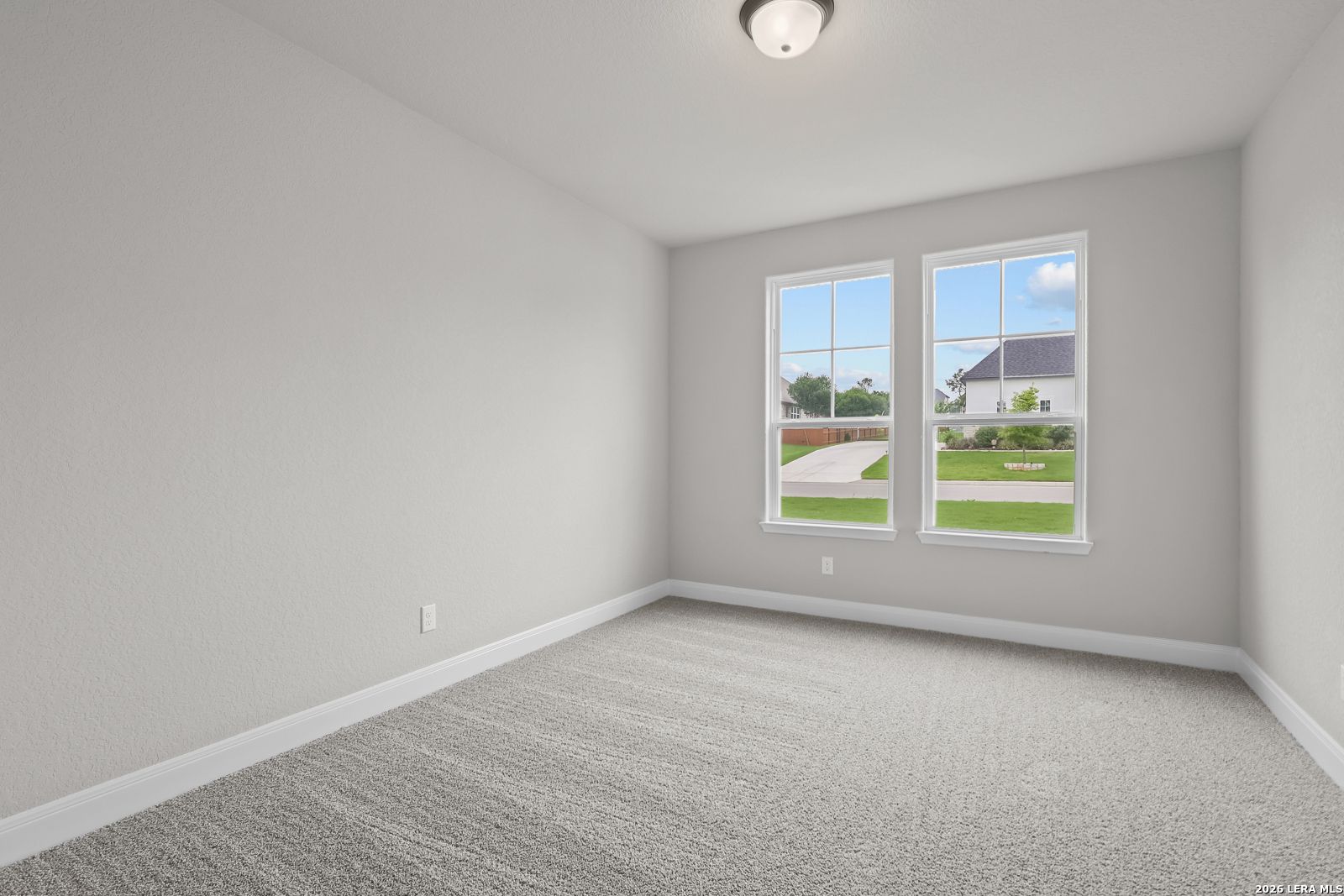 Empty bedroom with neutral gray walls, plush carpet, and large windows overlooking green lawn in Davidson Homes The Belmont H, Castroville Texas