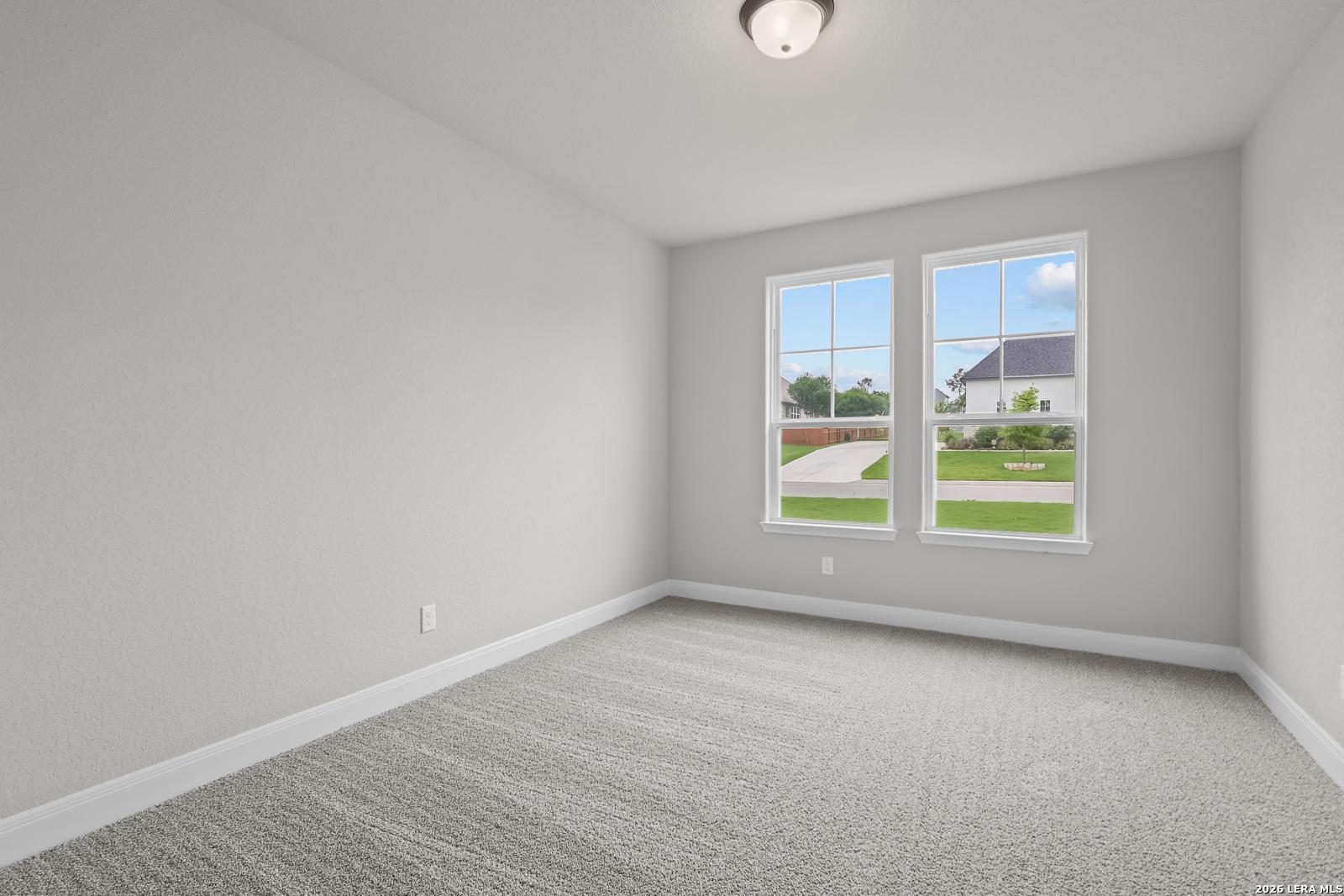Empty bedroom with neutral gray walls, plush carpet, and large windows overlooking green lawn in Davidson Homes The Belmont H, Castroville Texas