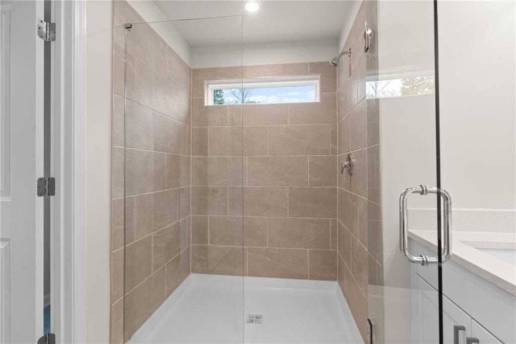 Modern frameless glass walk-in shower with beige tile walls, rainfall head, and window in master bath of Davidson Homes The Marion B, Kennesaw, GA