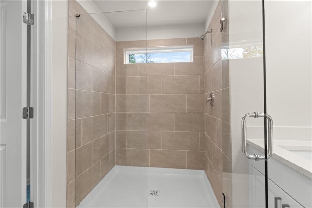 Modern frameless glass walk-in shower with beige tile walls, rainfall head, and window in master bath of Davidson Homes The Marion B, Kennesaw, GA