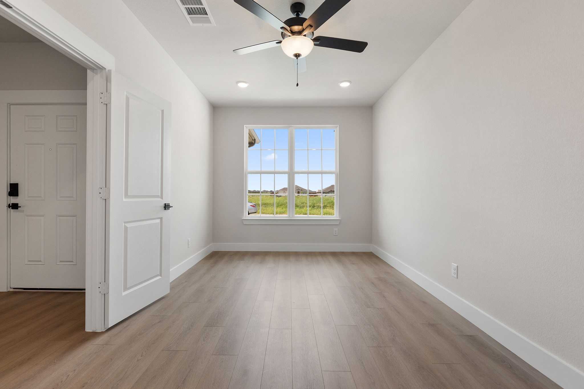 Bright secondary bedroom with hardwood floors, ceiling fan, and large window view of fields in Davidson Homes The Harrison D, Josephine, Texas