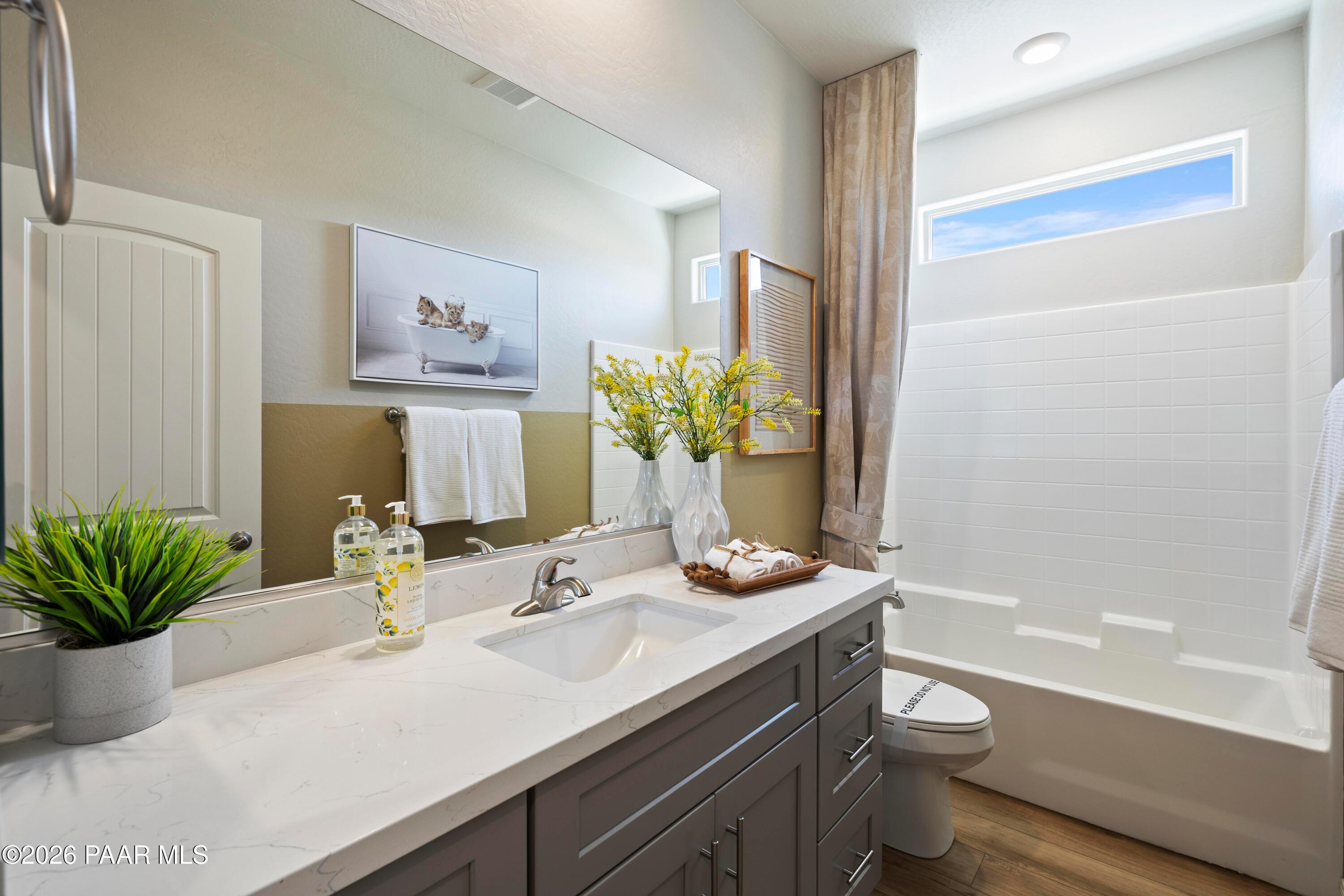 Modern bathroom with gray vanity, quartz countertop, and tub-shower combo in The Harmony A floor plan, Pronghorn Ranch.