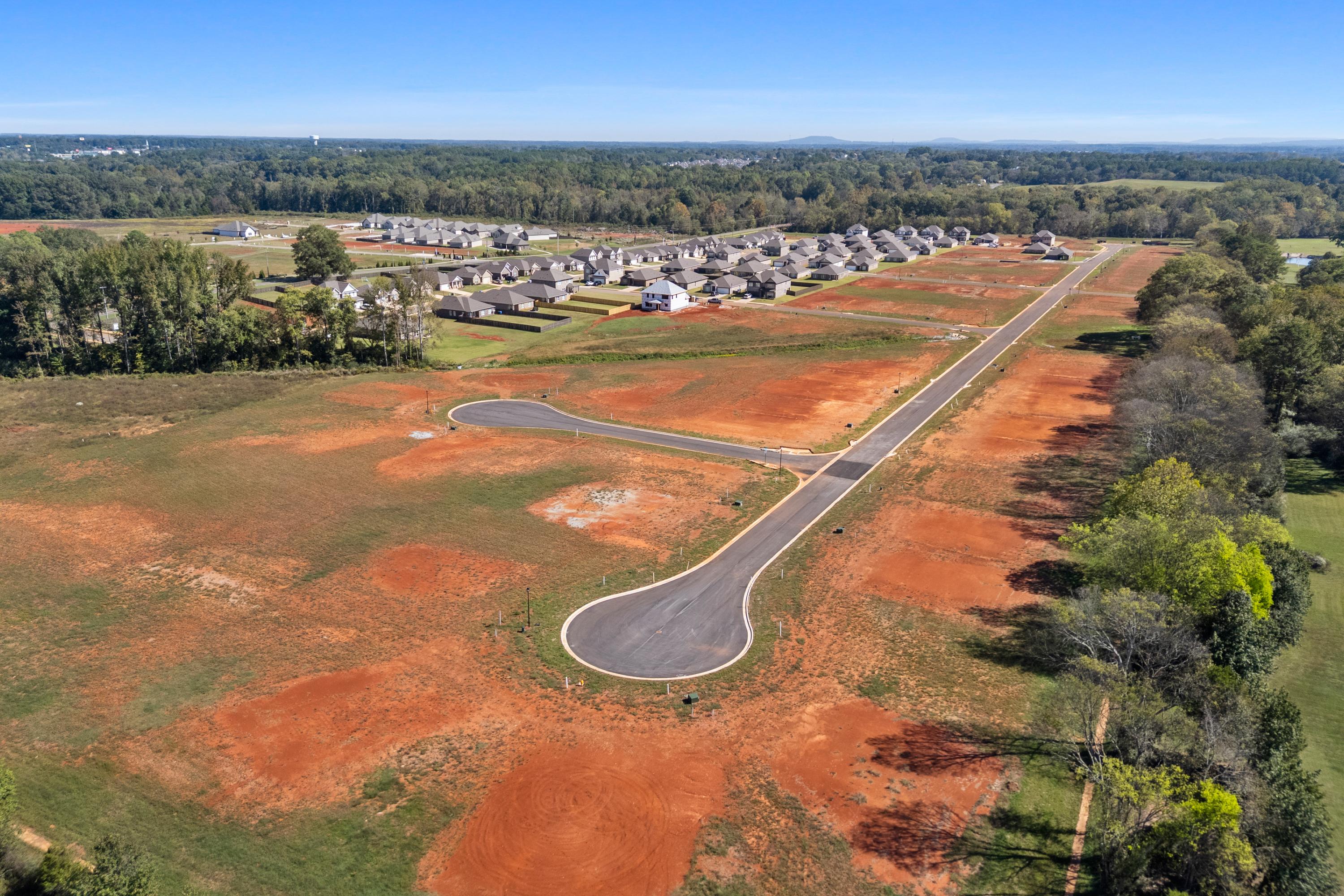 Aerial view of The Meadows neighborhood in Athens Alabama with new homes red dirt roads and wooded surroundings