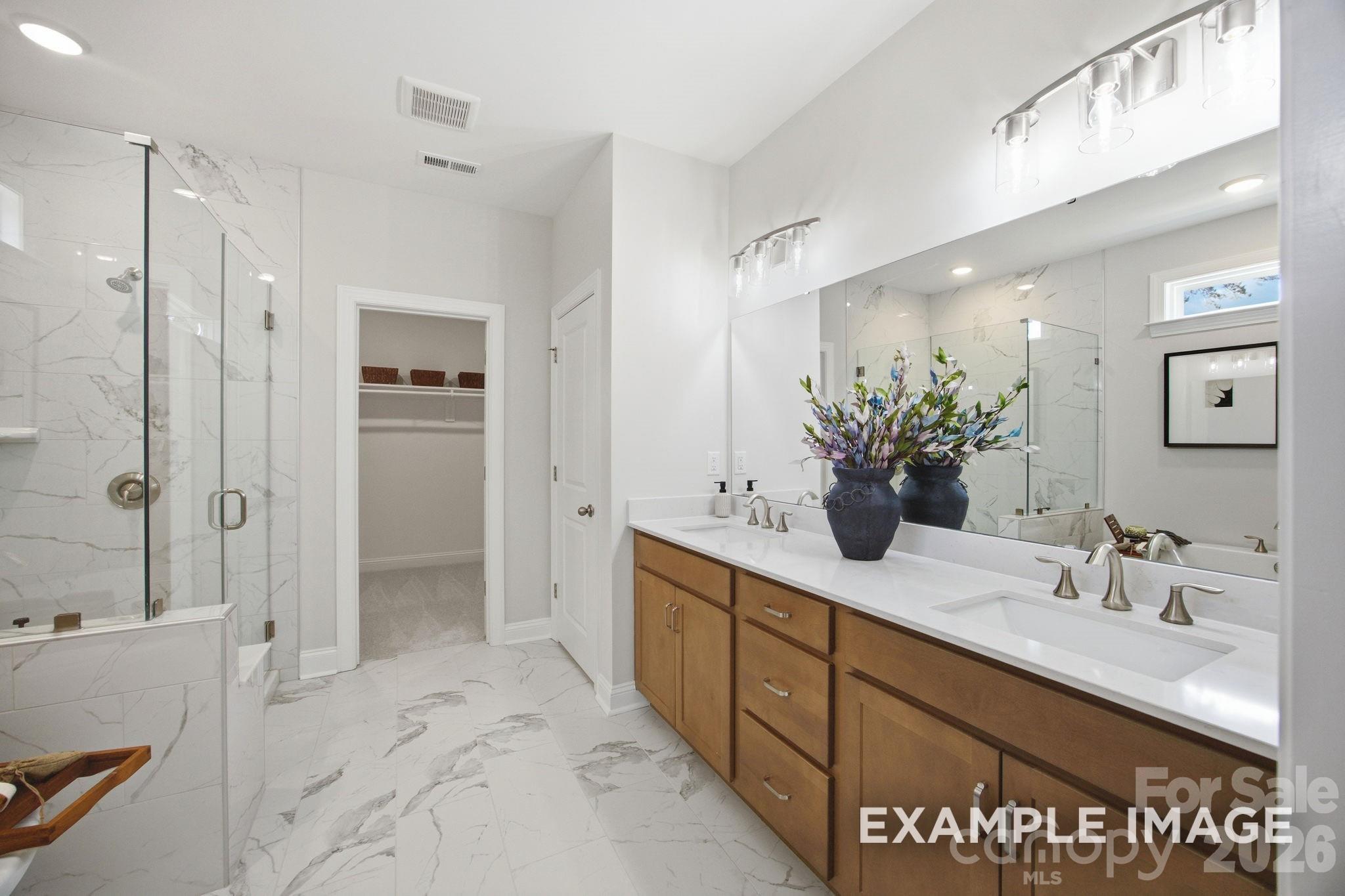 Modern primary bathroom with dual vanity, marble-style tile, and walk-in closet in The Hickory B II, Mooresville, NC.