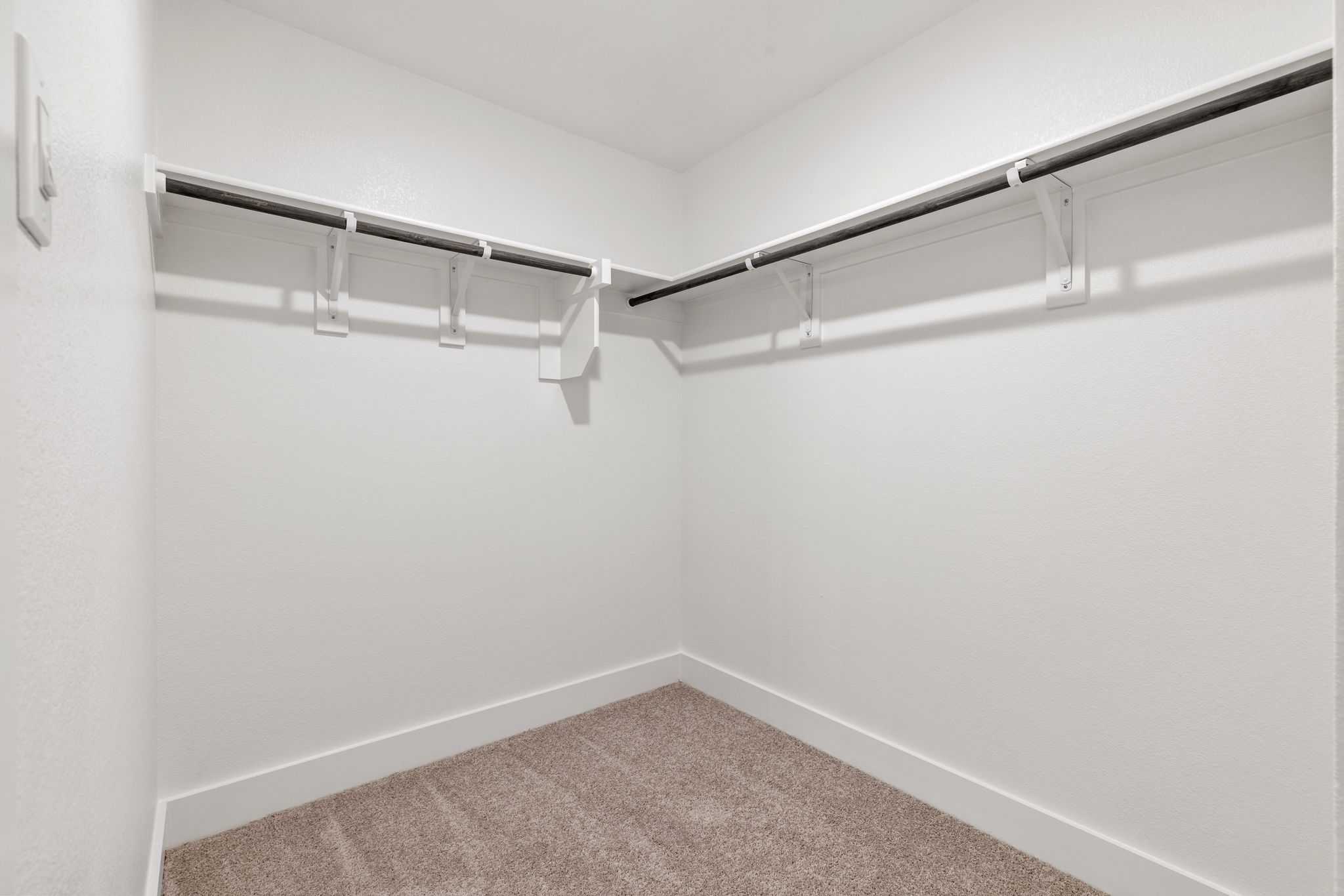Spacious walk-in closet with white walls, corner shelving, hanging rods, and carpet floor in Davidson Homes The Durham E, Wylie, Texas