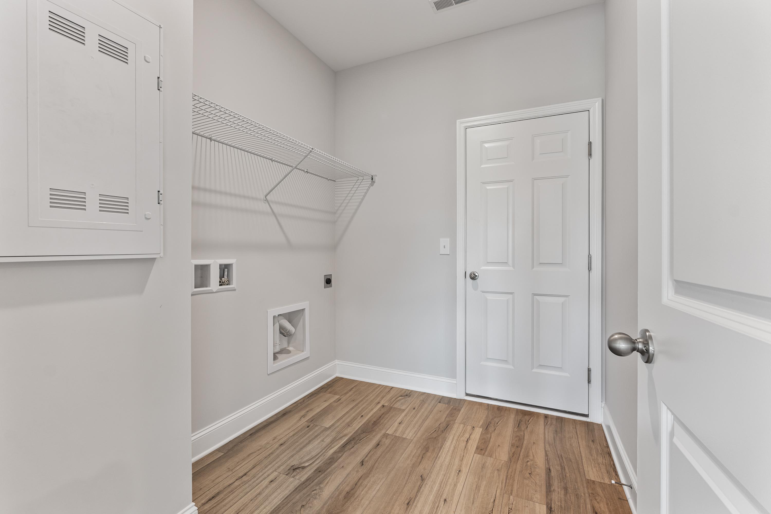 Spacious laundry room in The Butler by Davidson Homes with wire shelving, washer dryer hookups, white door, hardwood floors