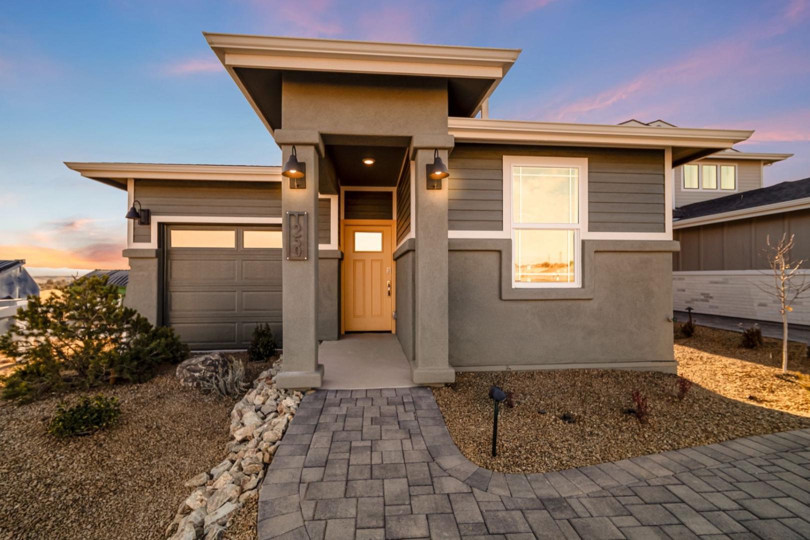 Modern single-story The Savannah A home elevation with gray stucco, attached garage, paver walkway, and desert rock landscaping at dusk in Prescott AZ