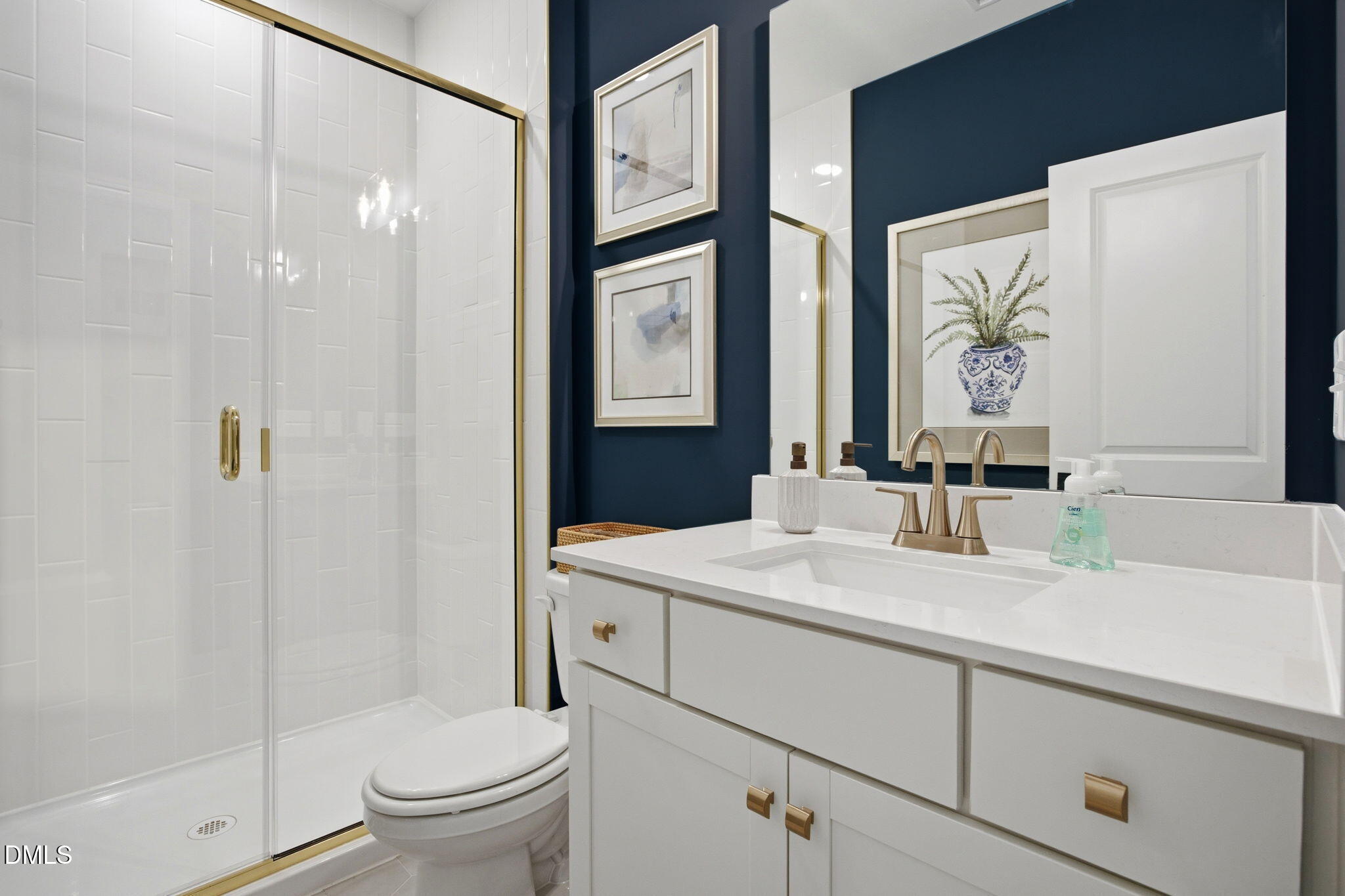 Modern bathroom with gold fixtures, white vanity, and glass shower in The Ashport M home at Wendell Ridge, North Carolina.