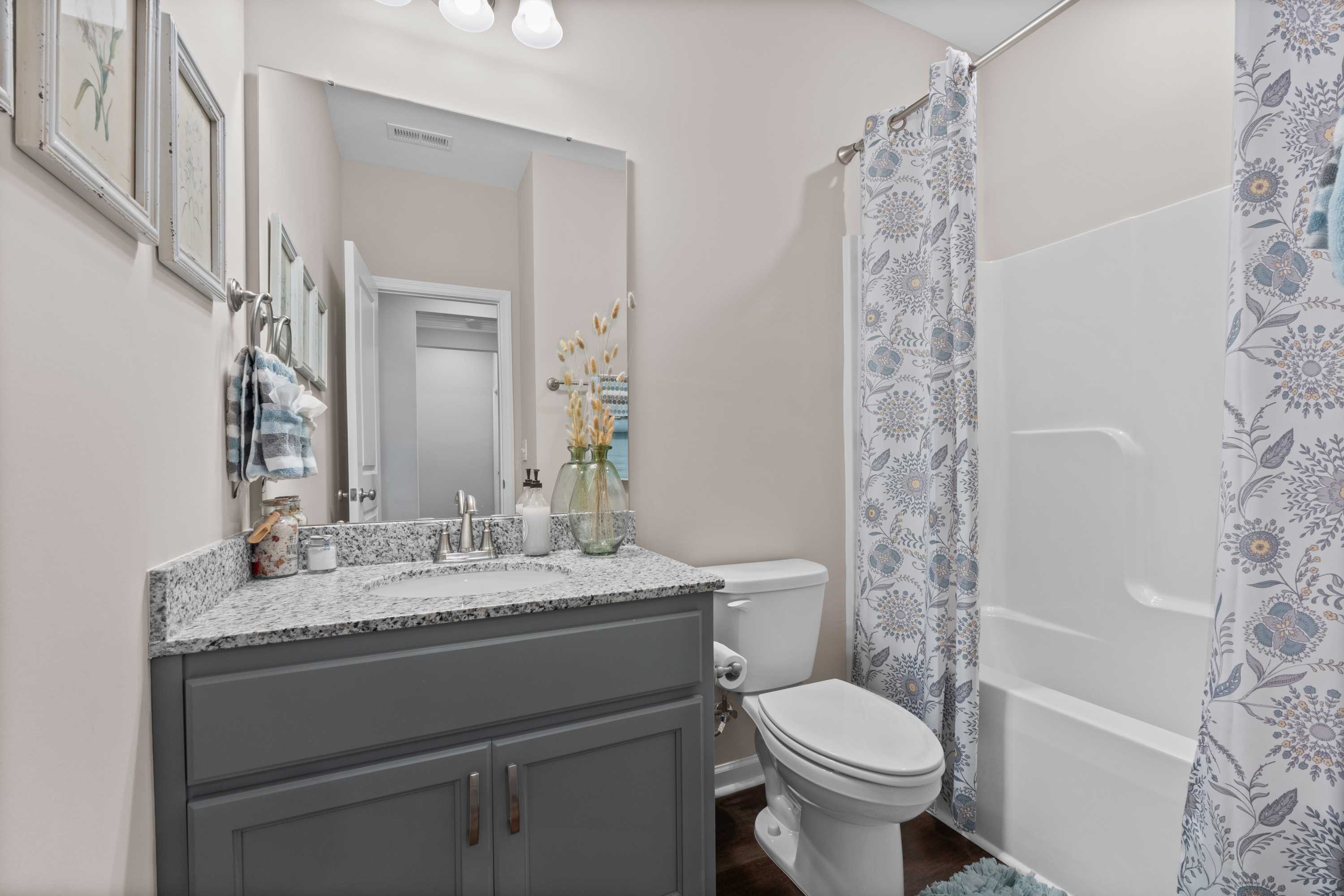 Spacious bathroom at Riverton Preserve in Huntsville AL with gray vanity, white tub shower combo, floral curtain, and soft beige walls