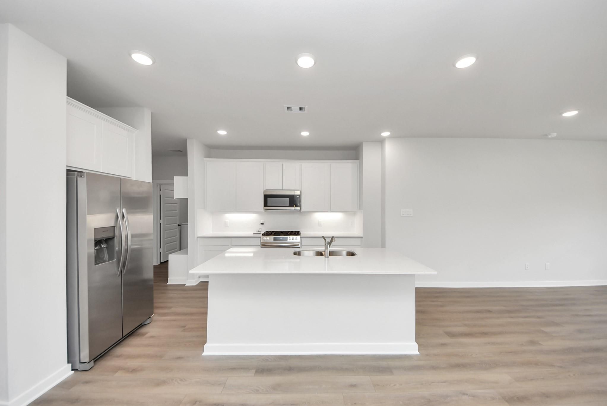 Modern open-concept kitchen with white cabinets, quartz island, and stainless appliances in The Blanco E at WestPointe.