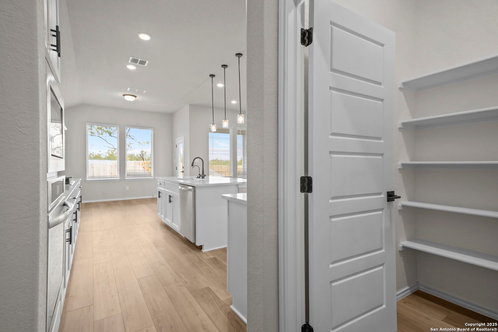 Bright kitchen with white cabinets, island sink, stainless appliances, and walk-in pantry in Davidson Homes Sequoia A, Converse Texas