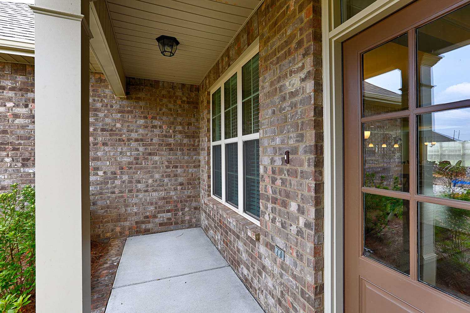 Charming brick exterior entrance of The Finleigh home with covered porch, wooden door, and large windows by Davidson Homes in Meridianville Alabama