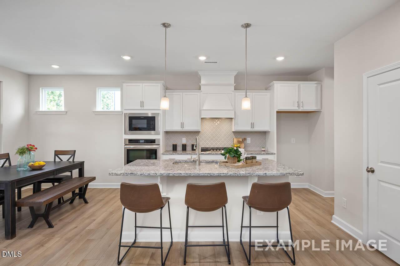 Open-concept kitchen with white cabinets, granite island, stainless appliances, and dining area in Davidson Homes The Willow D, Lillington, NC