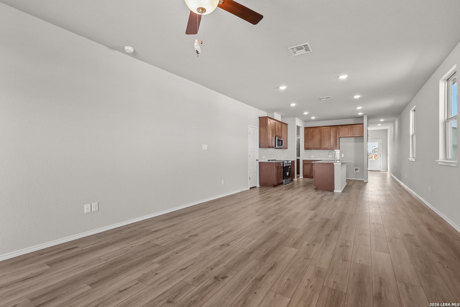Open-concept kitchen hallway with laminate wood floors, beige cabinets, ceiling fan in Davidson Homes The Frio B, San Antonio