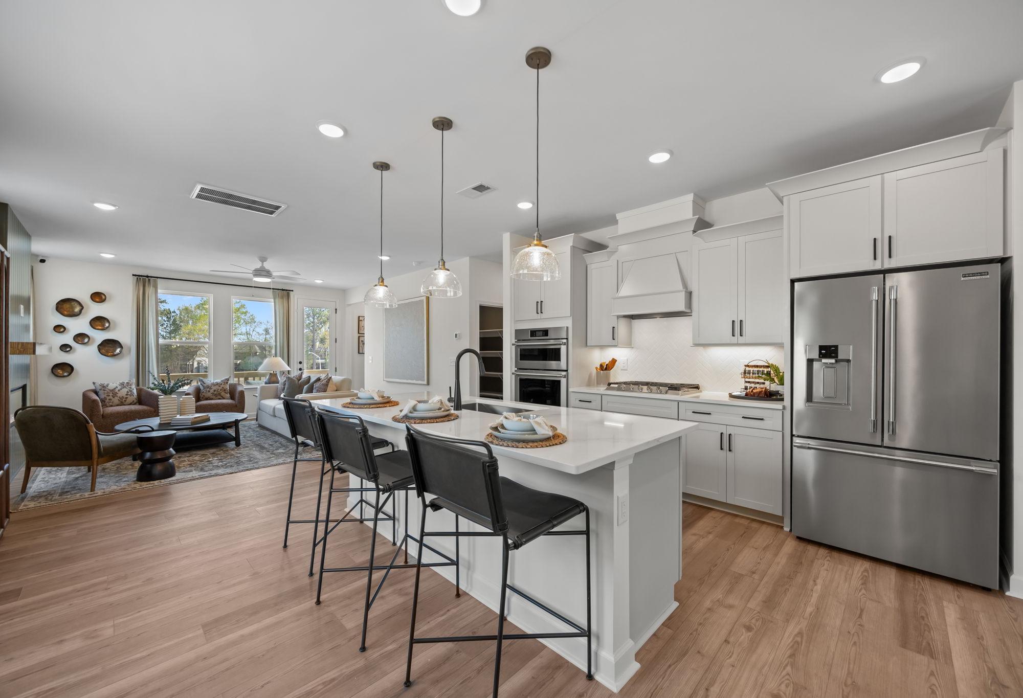 Open-concept kitchen and living area in The Mitchell featuring a central island, stainless appliances, and modern finishes.