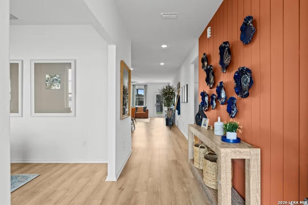 Elegant entry hallway with light wood floors, orange accent wall, blue ceramic art, and console table in Davidson Homes Douglas C, Converse, TX