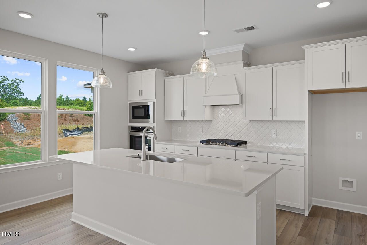 Modern kitchen with white cabinets, quartz island, and gas cooktop in The Chestnut floor plan at Wendell Ridge, NC.