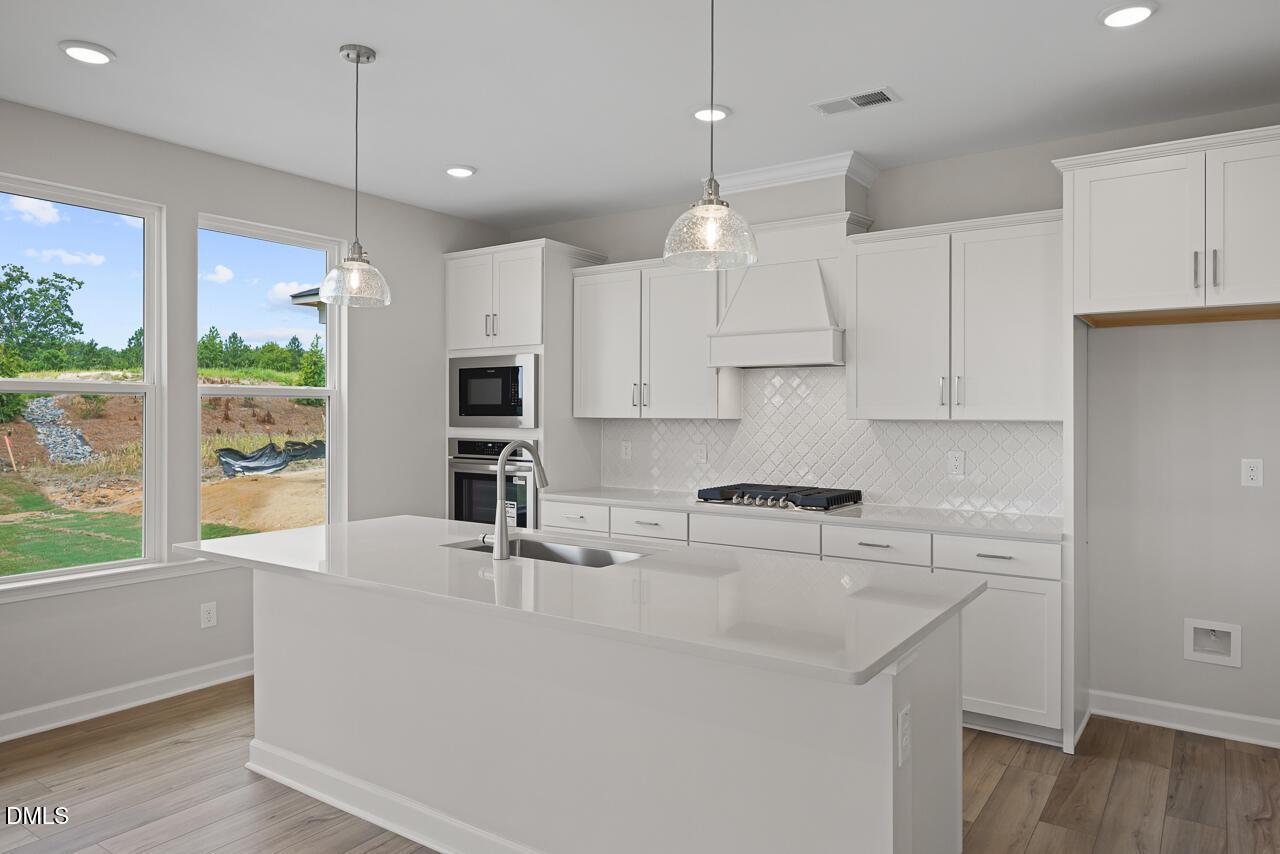 Modern kitchen with white cabinets, quartz island, and gas cooktop in The Chestnut floor plan at Wendell Ridge, NC.