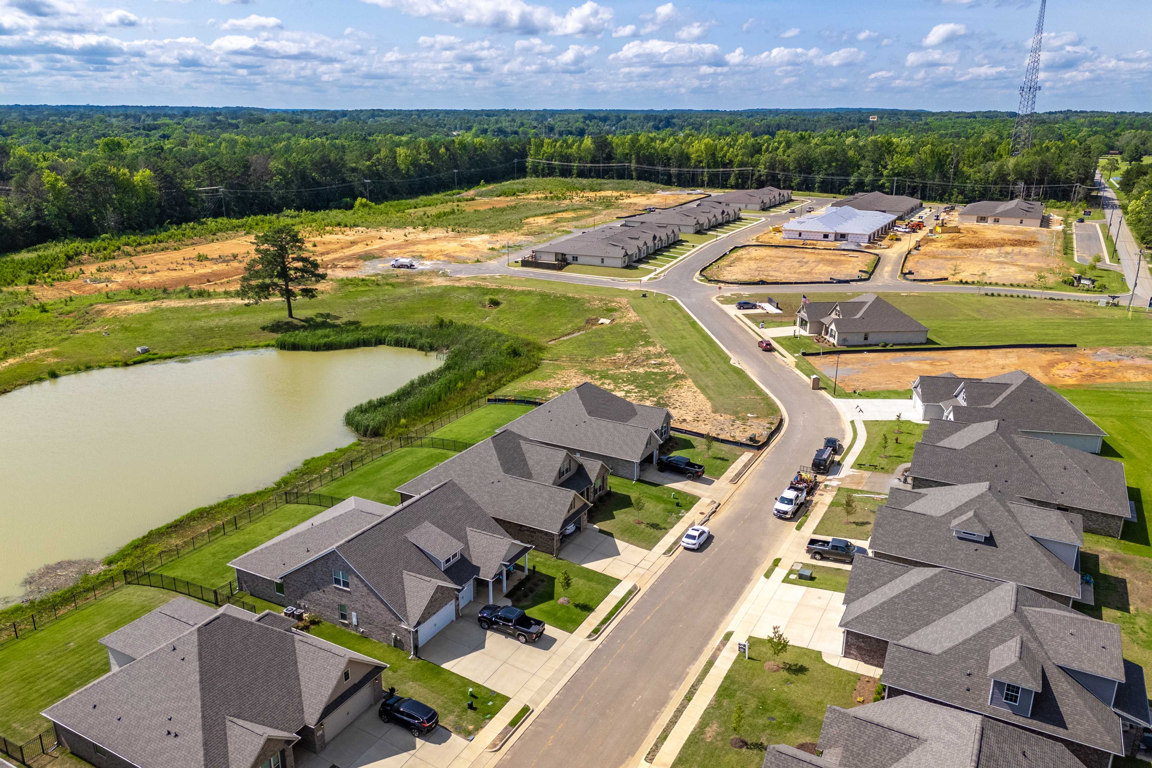 Aerial view of Cain Park neighborhood in Hartselle Alabama with new shingled-roof homes, retention pond, streets, and wooded surroundings