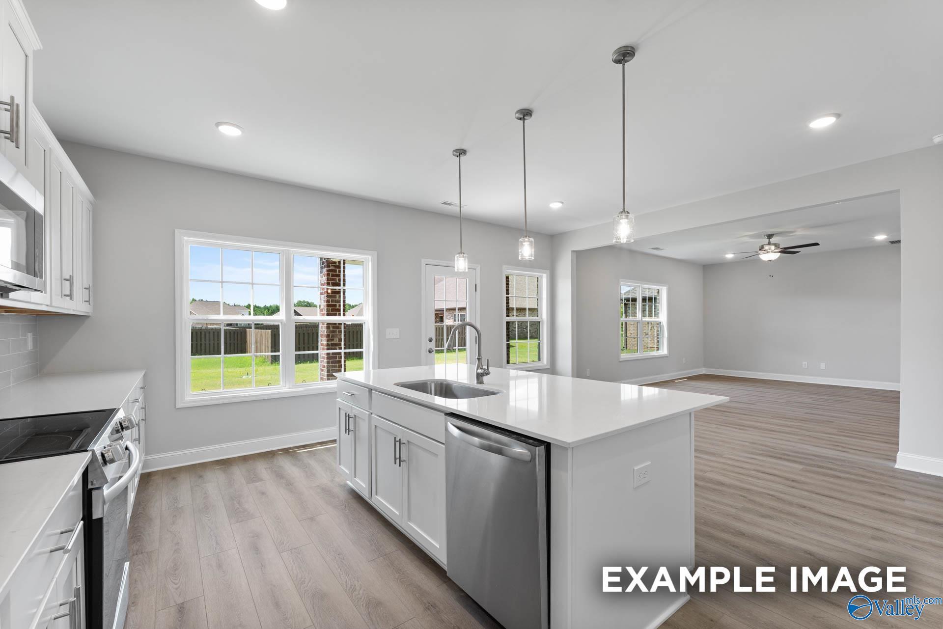 Modern kitchen with white island, stainless appliances, and open floor plan in The Madison A home, The Meadows, Athens, AL.