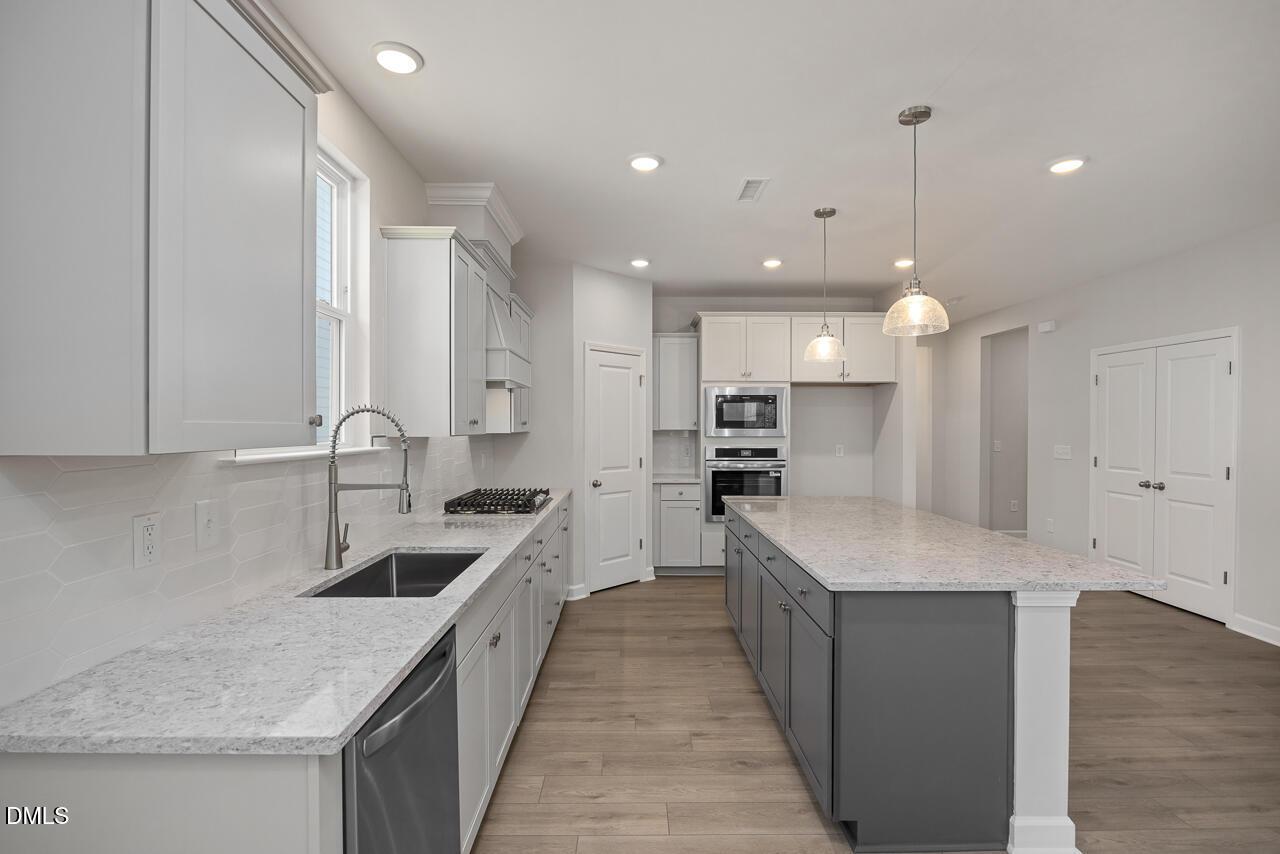 Modern kitchen with granite island, stainless appliances, and white cabinets in The Ashport G, Sage on North Main, Wake Forest