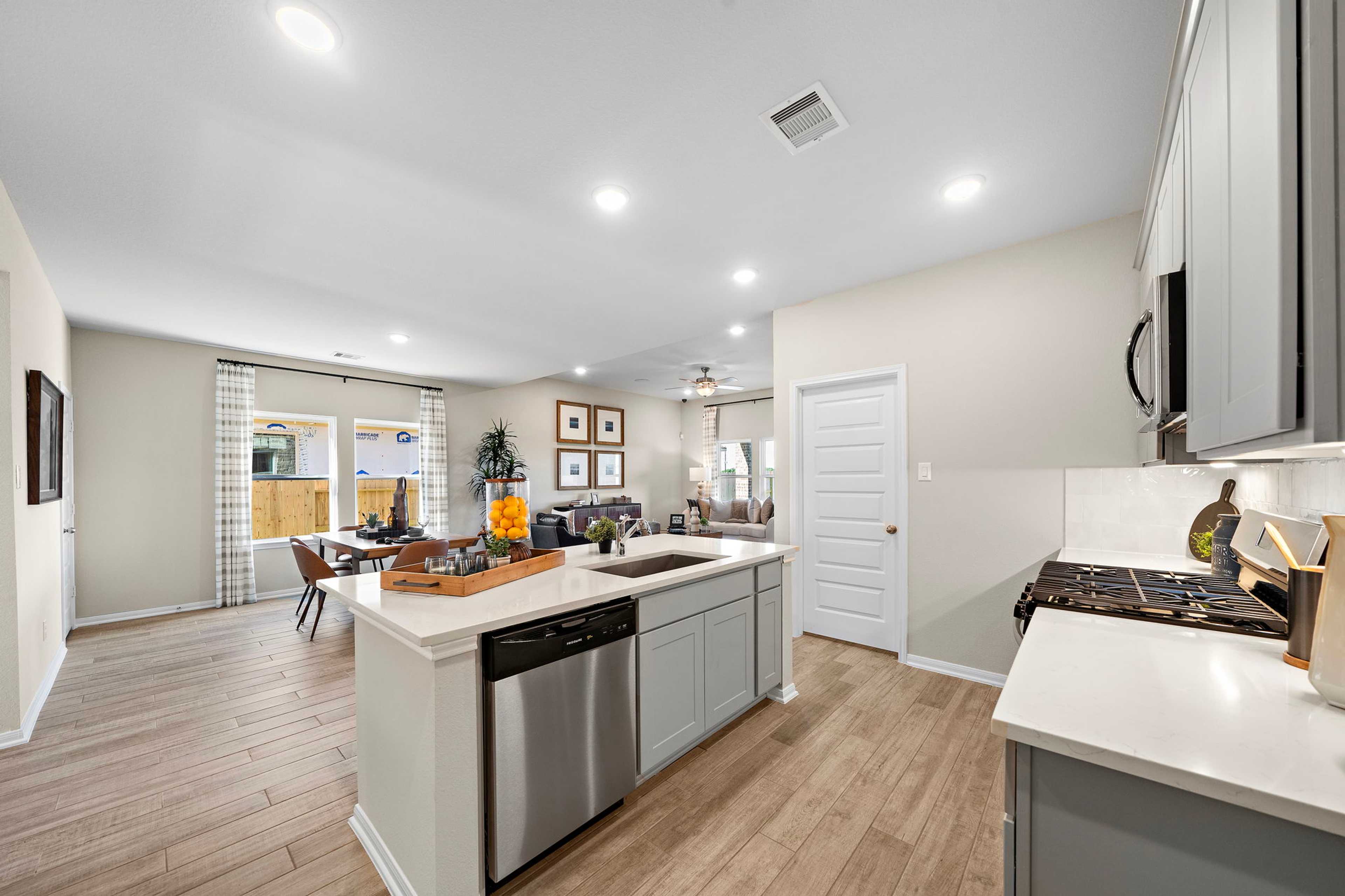 Spacious open-concept kitchen living room at Emberly in Beasley Texas with gray cabinets quartz island hardwood floors